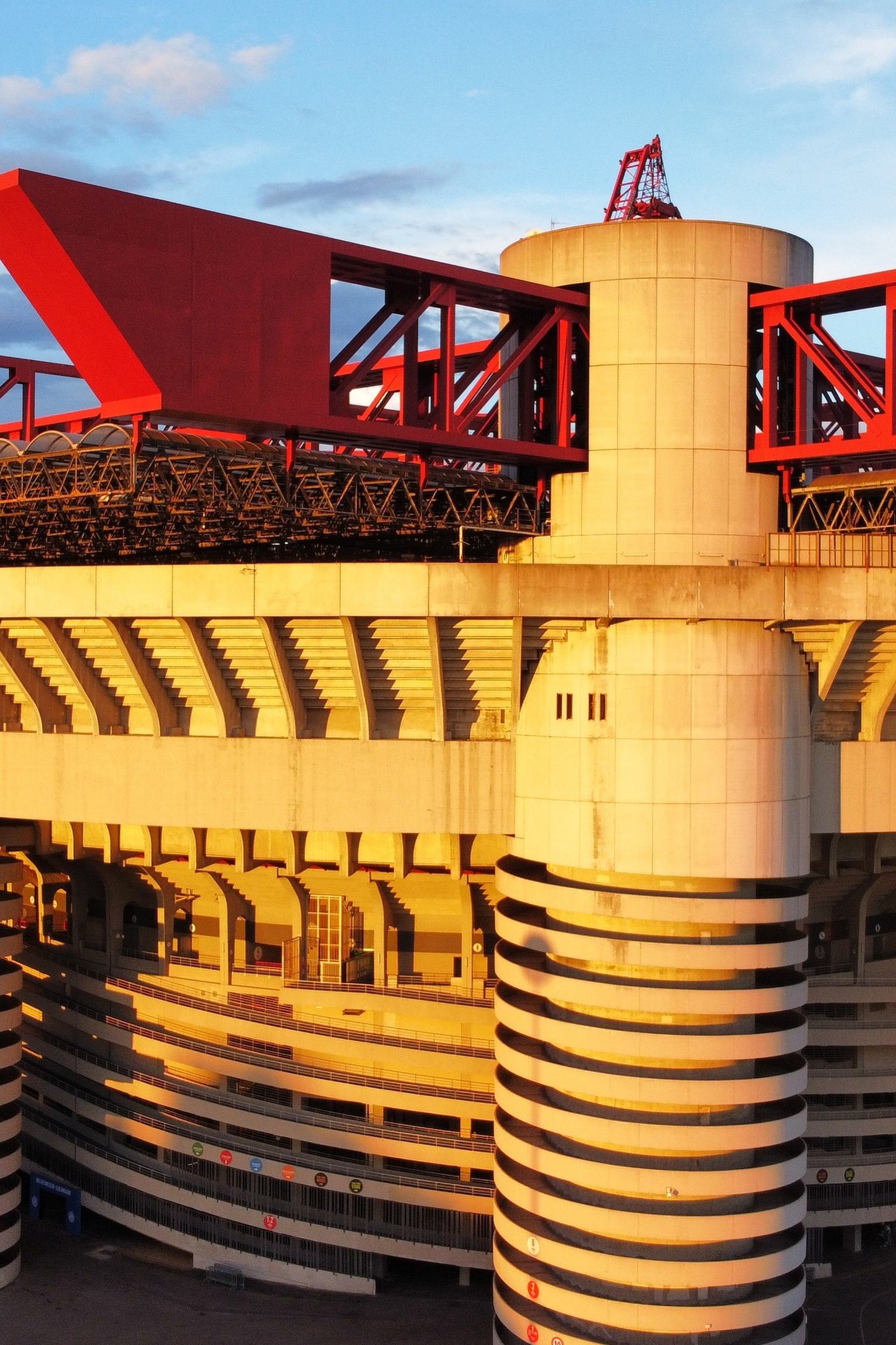 A Brutalist stadium with red roof structures and spiral concrete ramps, illuminated by golden hour sunlight.