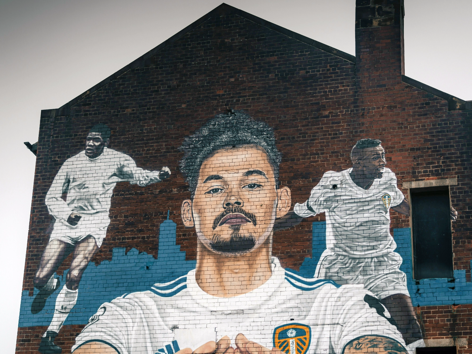 Mural dos jogadores de futebol do Leeds United Kalvin Phillips, Albert Johanneson e Lucas Radebe em um prédio de tijolos.