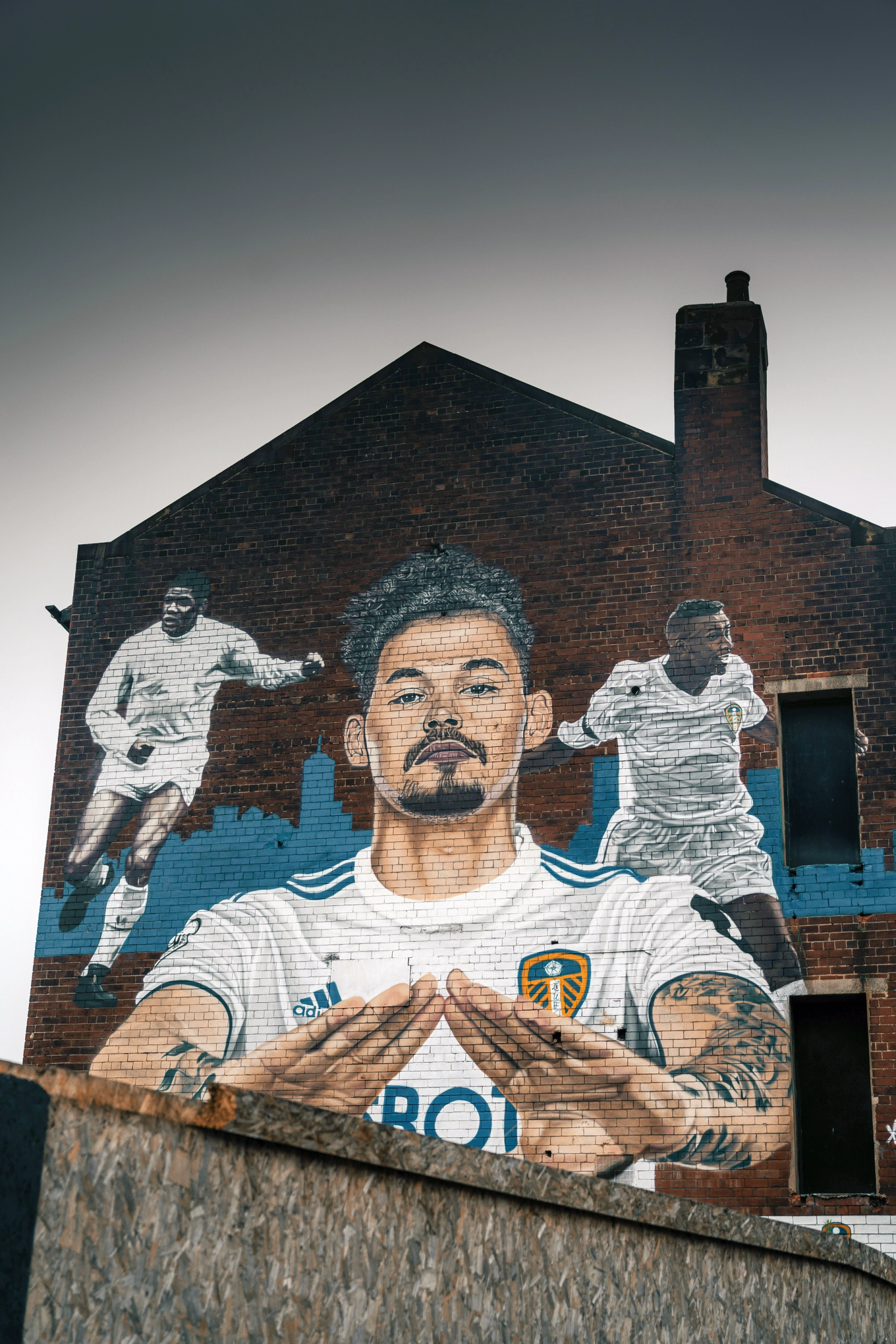 Mural dos jogadores de futebol do Leeds United Kalvin Phillips, Albert Johanneson e Lucas Radebe em um prédio de tijolos.