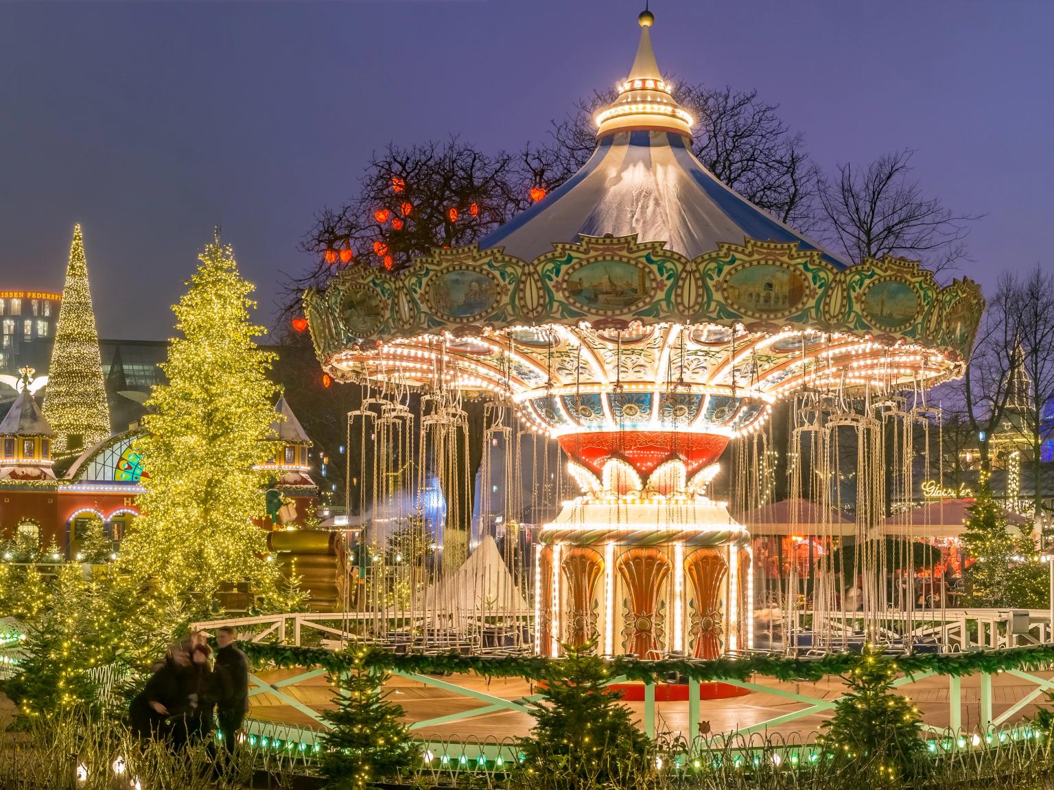 En festlig forlystelsespark om natten med en lyst op karrusel, juletræer og dekorerede bygninger.