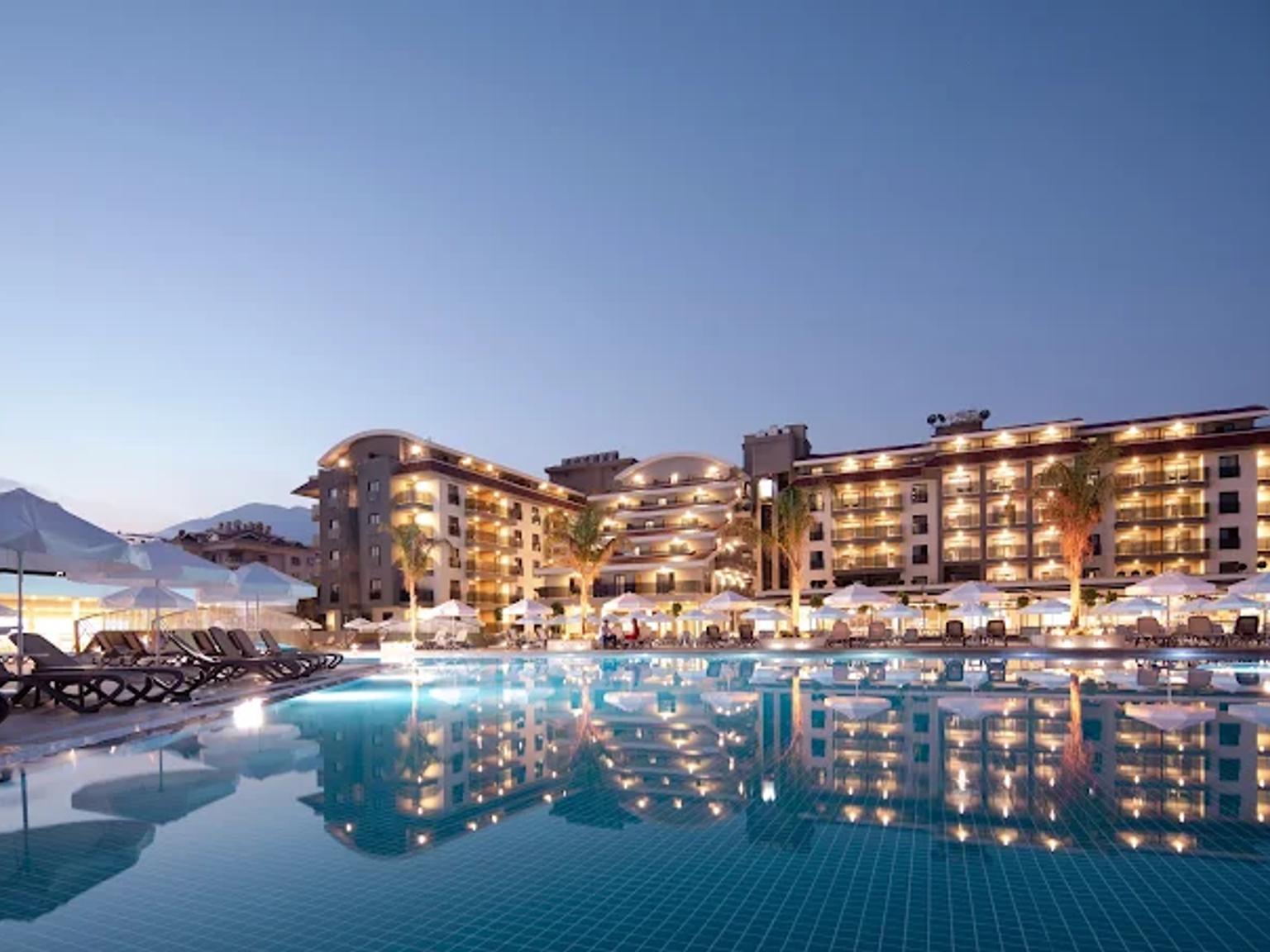 En oplyst hotelbygning og stor swimmingpool i skumringen, med lys der reflekteres i vandet og liggestole. Green Garden Resort & Spa Hotel, Alanya