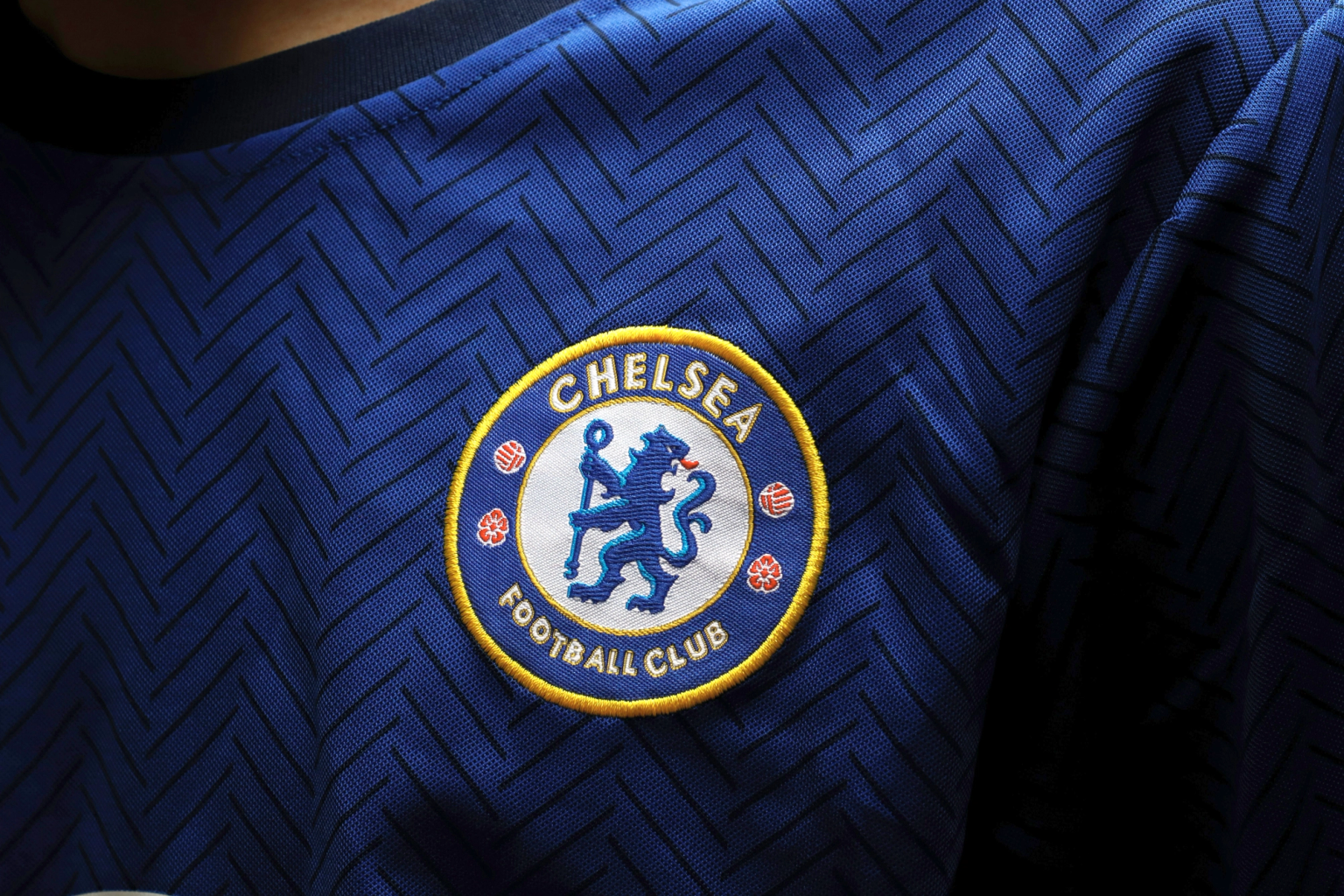 Close-up of the Chelsea Football Club logo embroidered on a blue jersey with a chevron pattern.