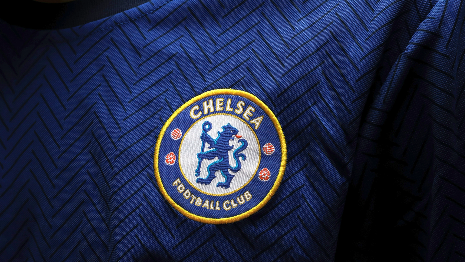 Close-up of the Chelsea Football Club logo embroidered on a blue jersey with a chevron pattern.