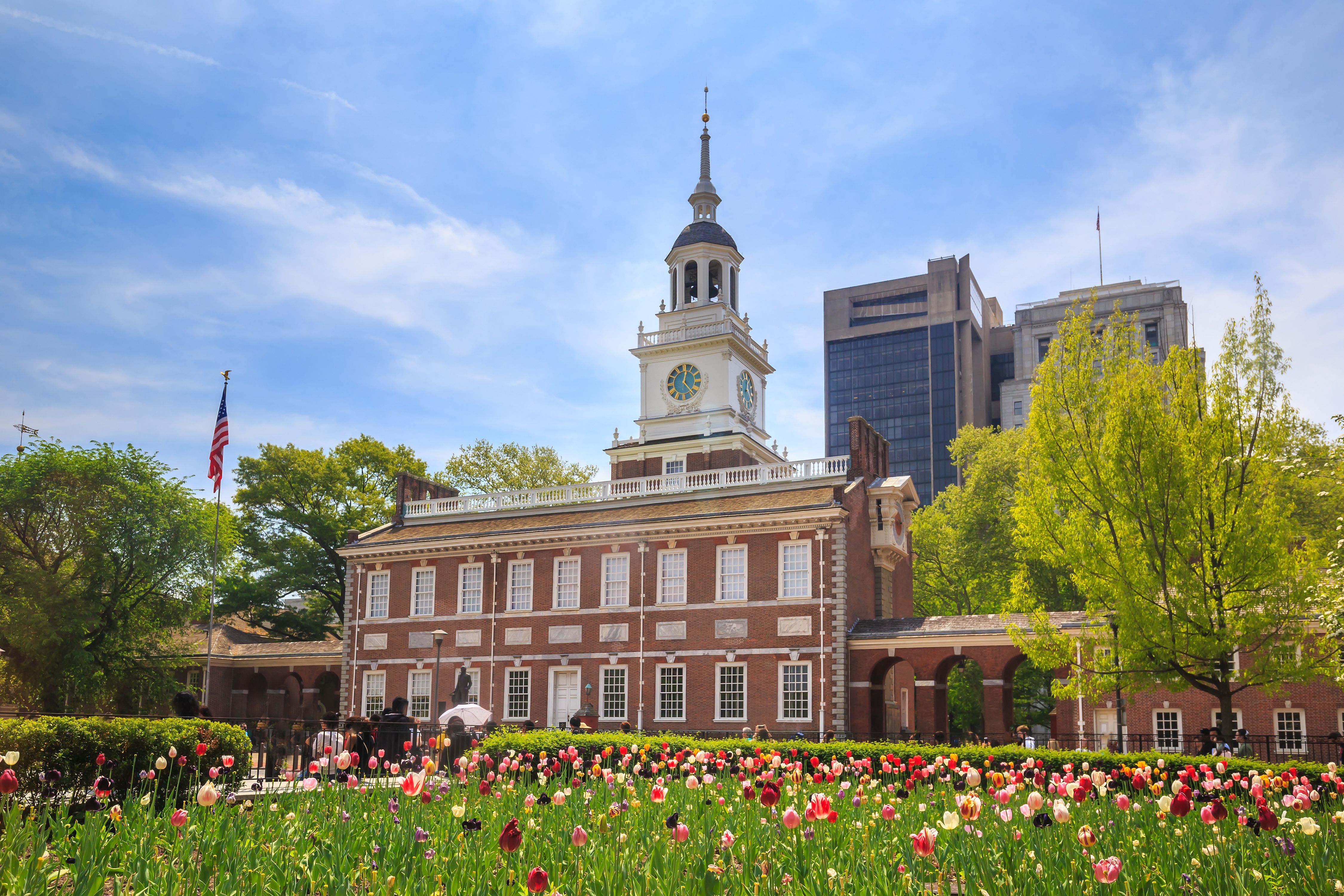 Independence Hall med et amerikansk flag og en mark med farverige tulipaner under en blå himmel. Philadelphia