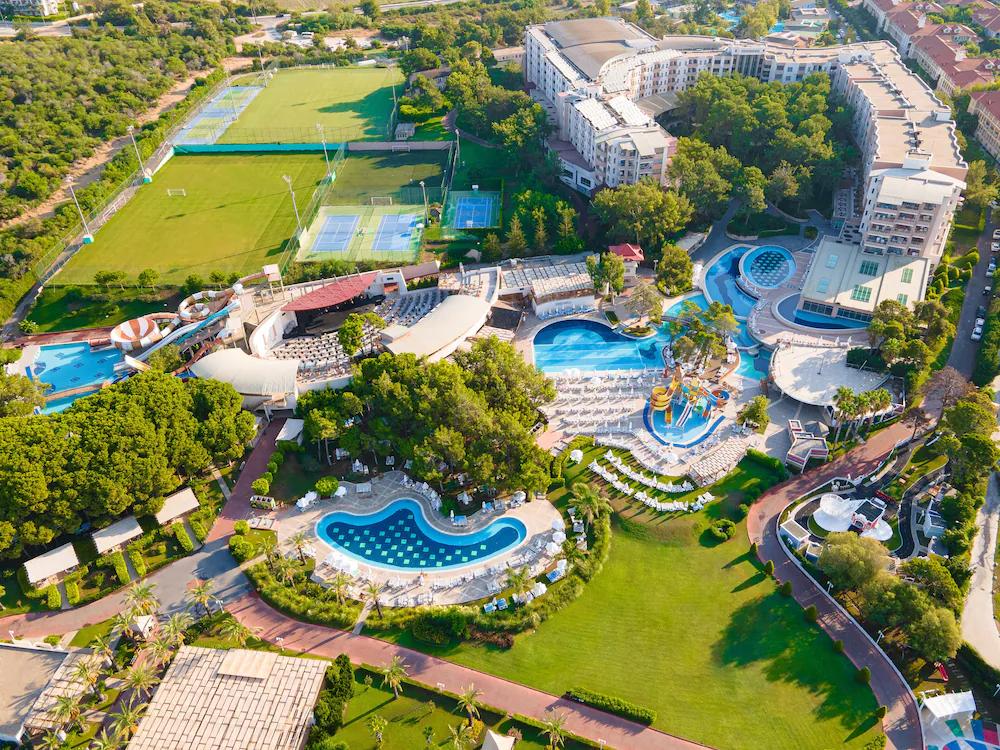 Aerial view of a large resort complex featuring multiple swimming pools, water slides, sports fields, and buildings amidst lush greenery. Sueno Hotels Beach Side