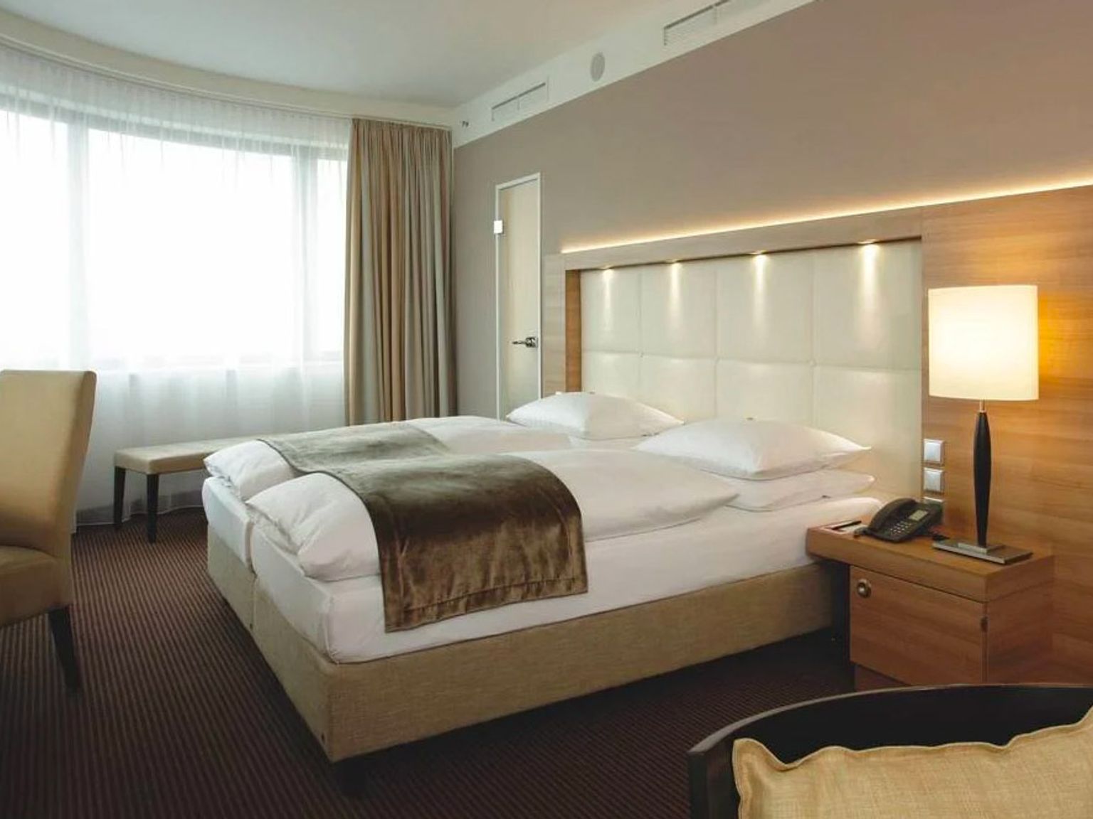 ett hotellrum med en säng, stol, nattduksbord, lampa och fönster