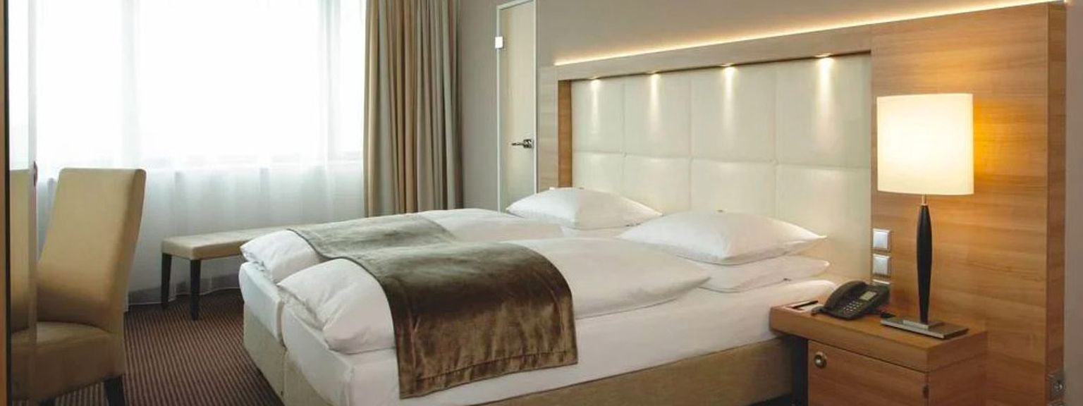 ett hotellrum med en säng, stol, nattduksbord, lampa och fönster