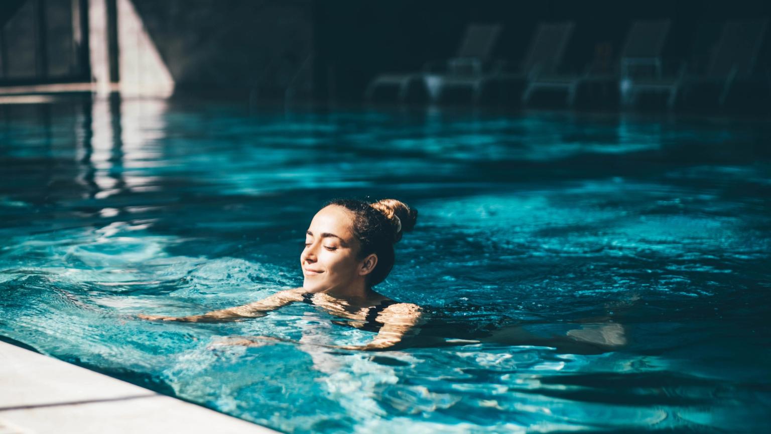 En kvinna med slutna ögon slappnar av i en blå swimmingpool.
