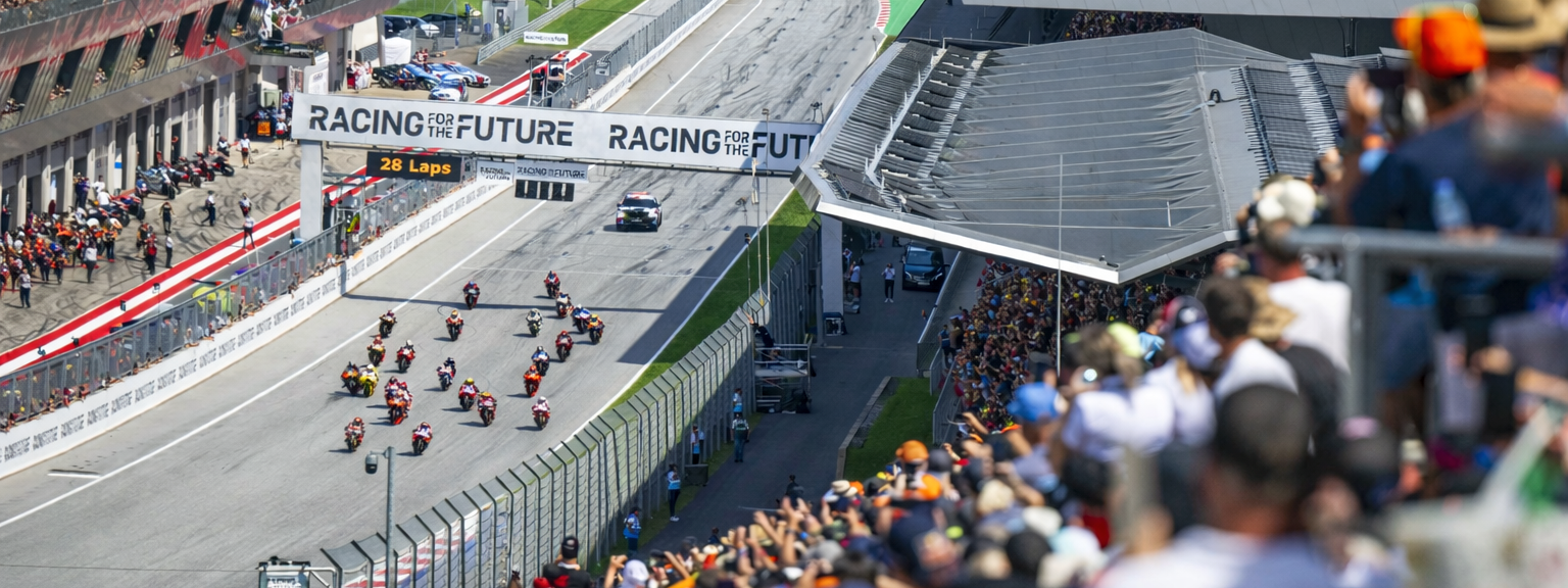Motorfietsen racen op het circuit van de Red Bull Ring, terwijl toeschouwers de tribunes vullen.