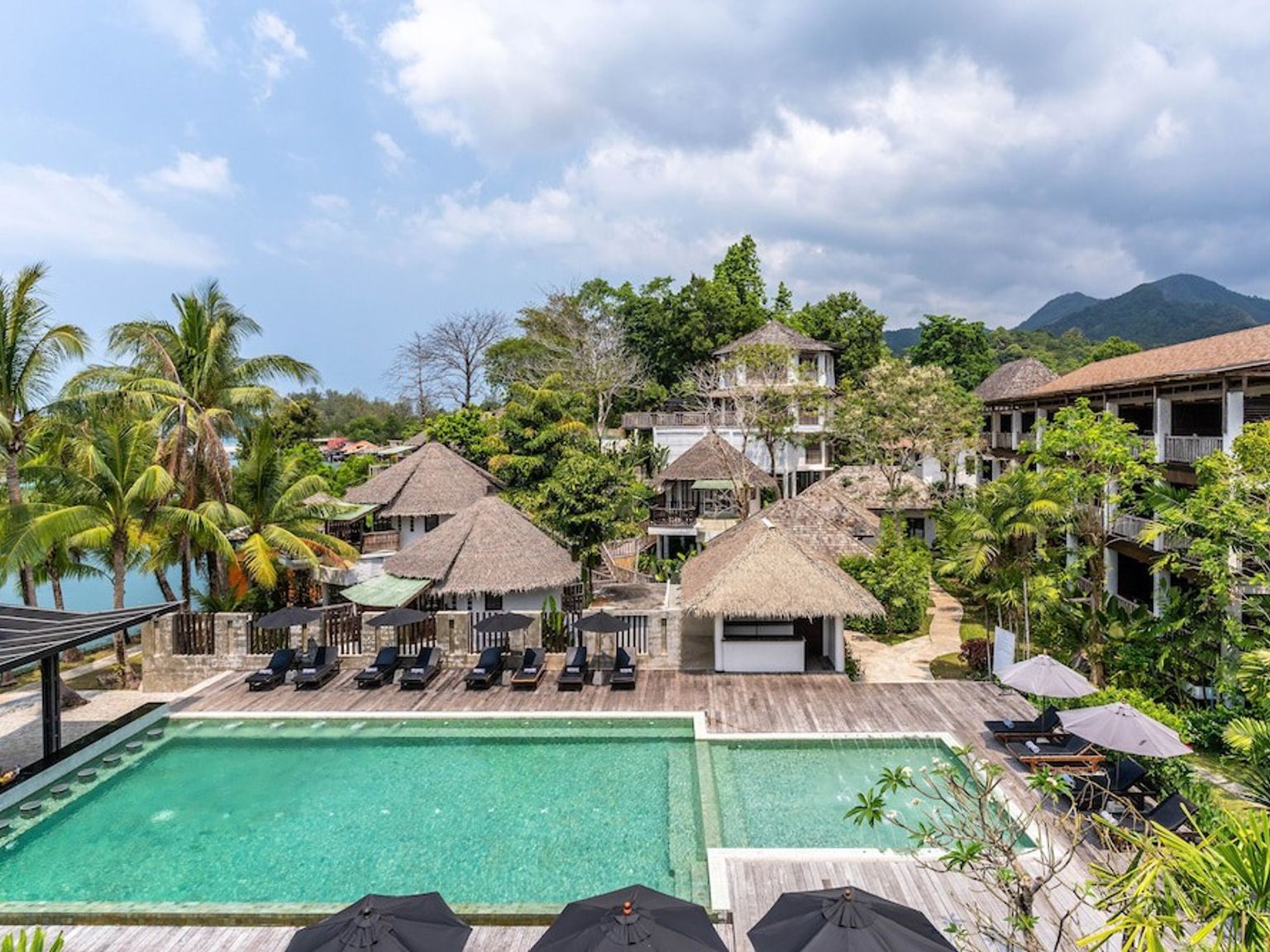 een groot zwembad omgeven door stoelen en parasols in een tropisch resort