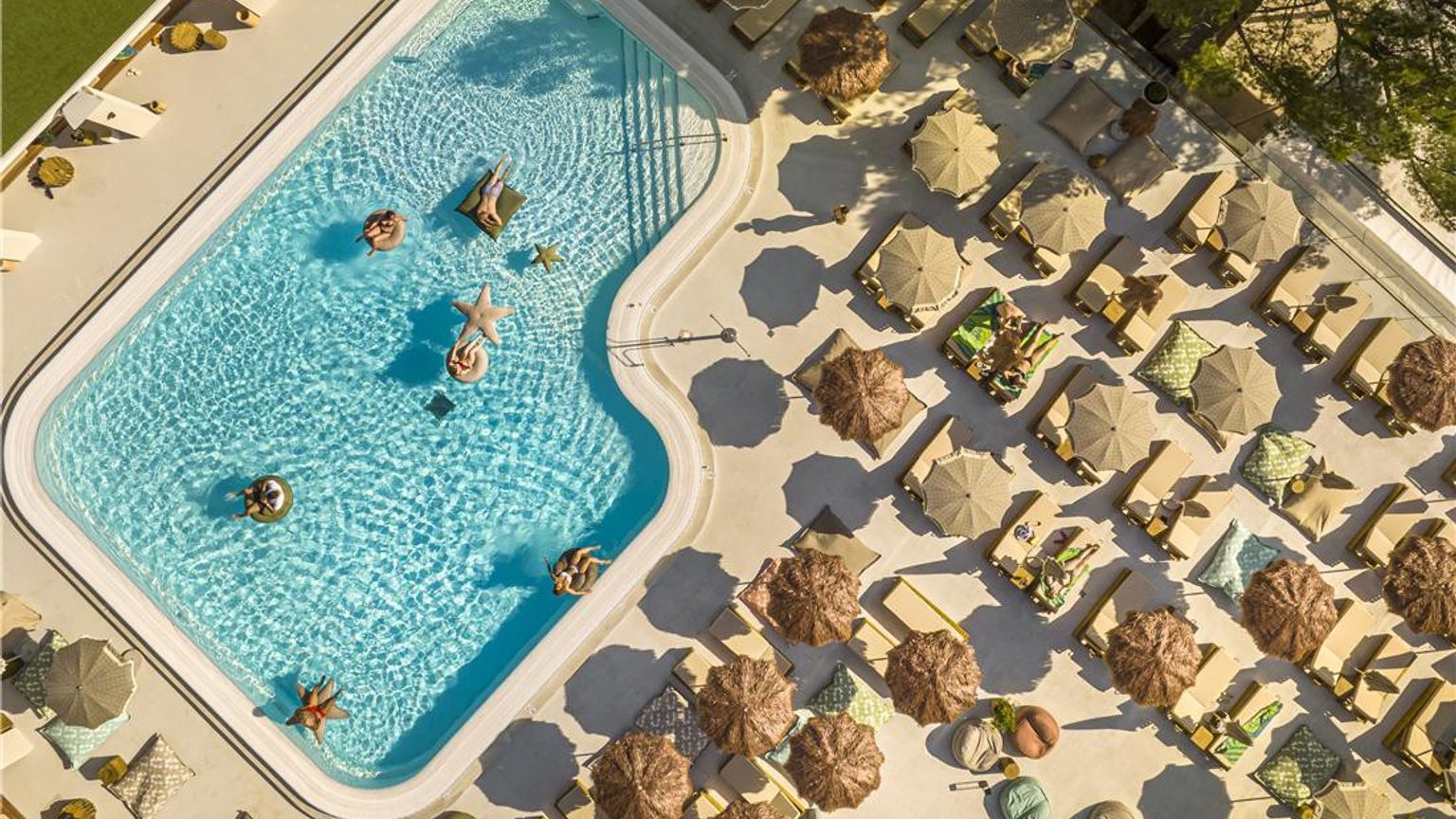 Vue aérienne d’une piscine de complexe hôtelier avec des personnes sur des bouées et une terrasse bordée de chaises longues et de parasols. Dalmacija Places Hotel by Valamar