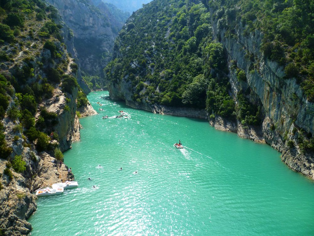 En livlig turkos flod med båtar och simmare rinner genom en brant, grön kanjon. Gorges du Verdon, Frankrike