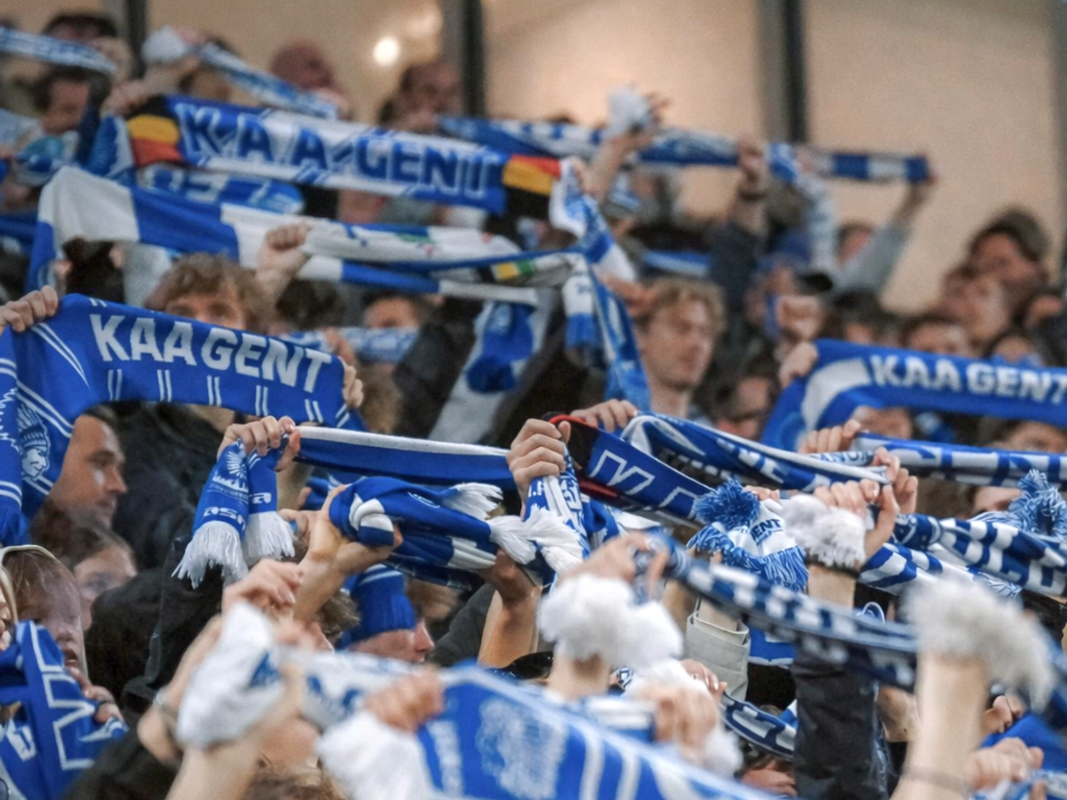 Eine große Menge von KAA-Gent-Fans, die blau-weiße Schals in die Höhe halten.