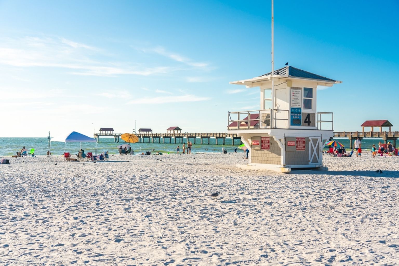 LivreddertÄrn pÄ en hvit sandstrand med en brygge, mennesker og blÄ himmel. Clearwater Beach, Florida