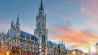 Münchens neugotisches Neues Rathaus am Marienplatz, beleuchtet in der Dämmerung unter einem bunten Himmel.