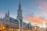 Münchens neugotisches Neues Rathaus am Marienplatz, beleuchtet in der Dämmerung unter einem bunten Himmel.