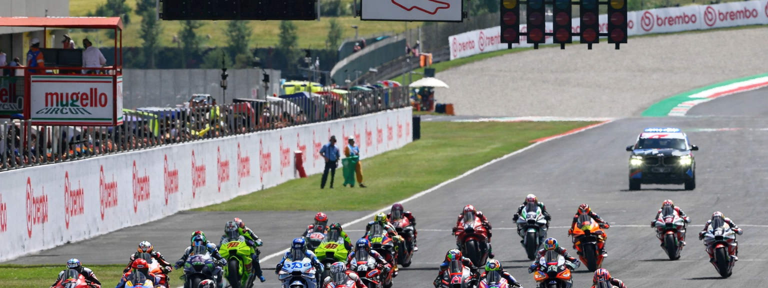 Motorfietsen racen over het Mugello Circuit met zichtbare Brembo-banners en startlichten.