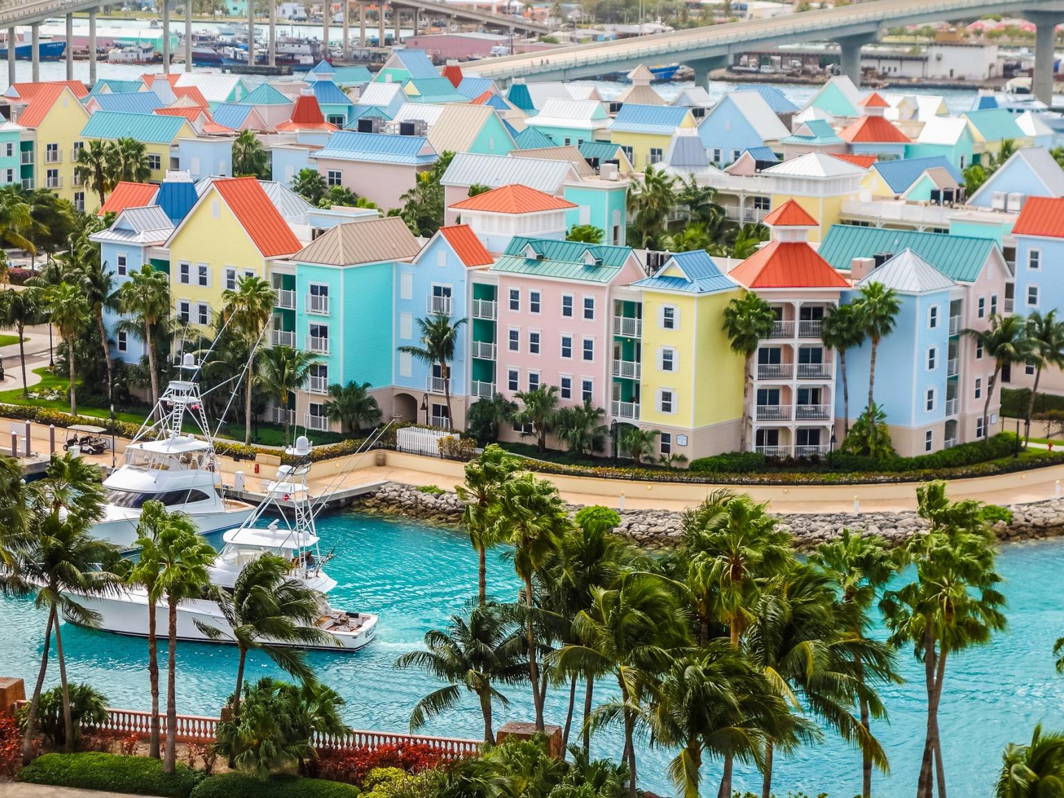 en båt är förtöjd framför en rad färgglada byggnader på en tropisk ö.