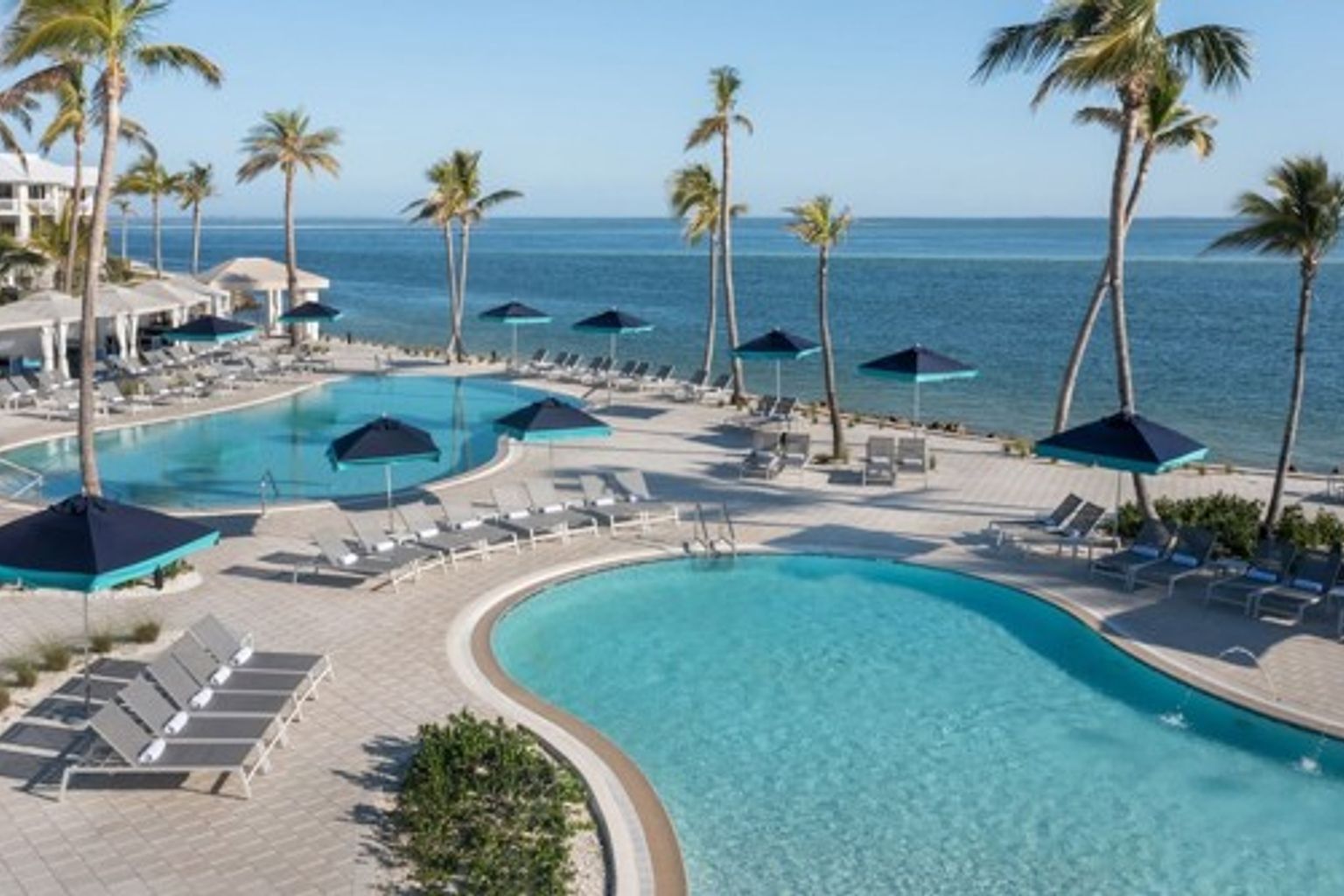 et stort svømmebasseng omgitt av stoler og parasoller ved siden av havet