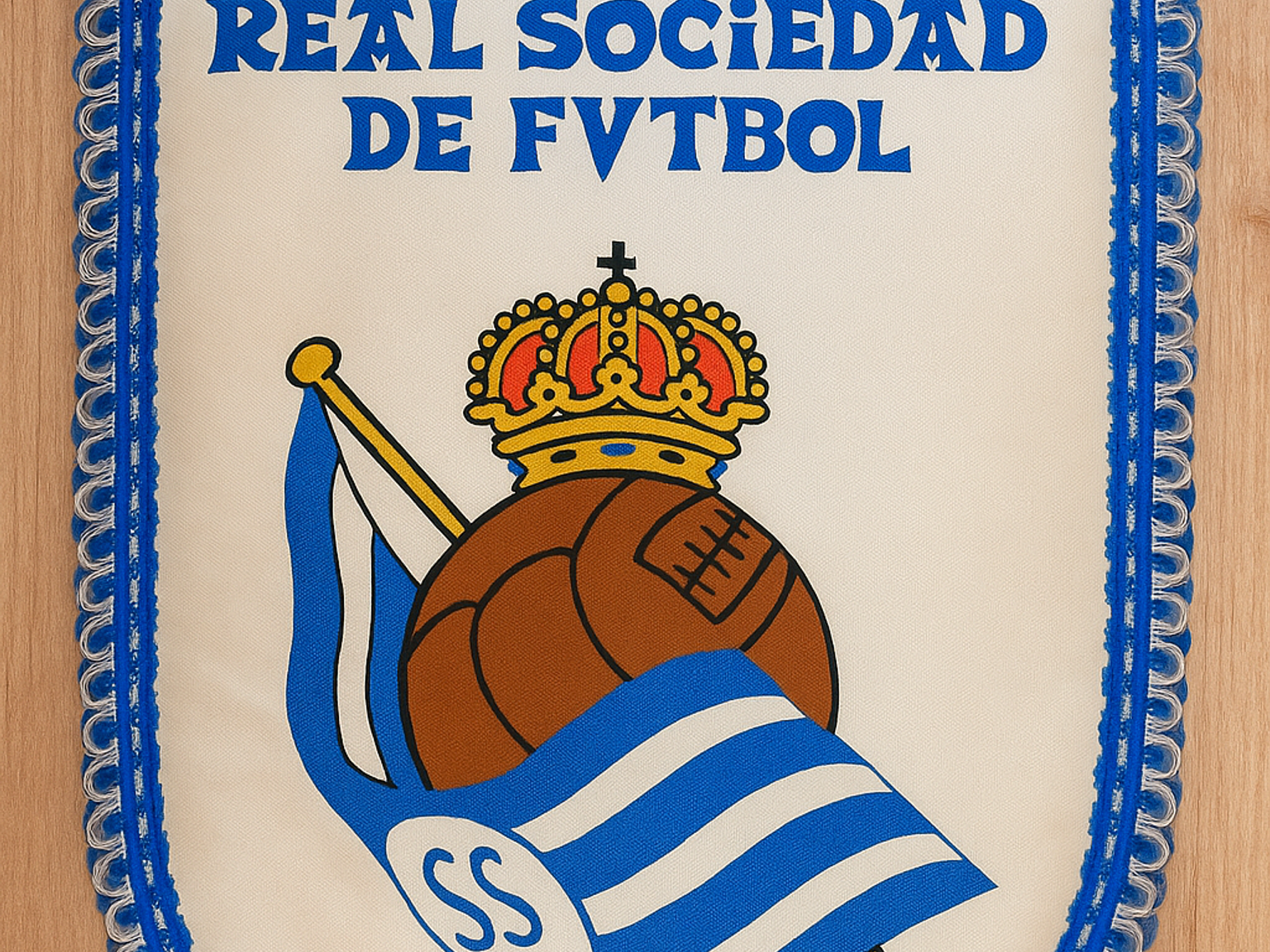 A cream-colored Real Sociedad de Futbol pennant with blue trim, featuring a crowned brown football and a blue and white striped flag with "SS".
