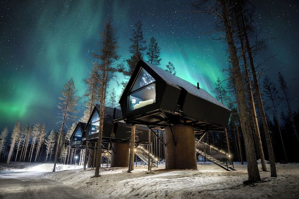 Moderna stugor på pålar i en snöig skog under norrskenet. Aito Igloo & Spa Resort