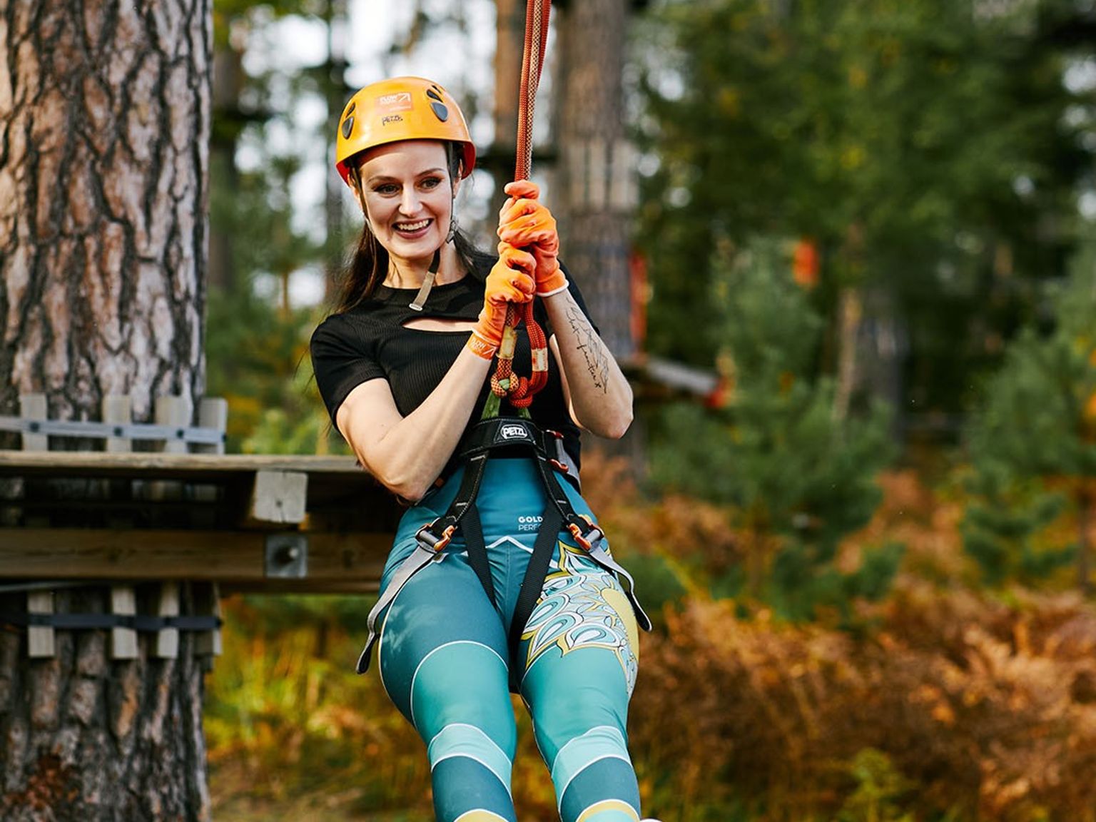 Hymyilevä nainen liitää vaijeriliukua puiden latvojen seikkailupuistossa.