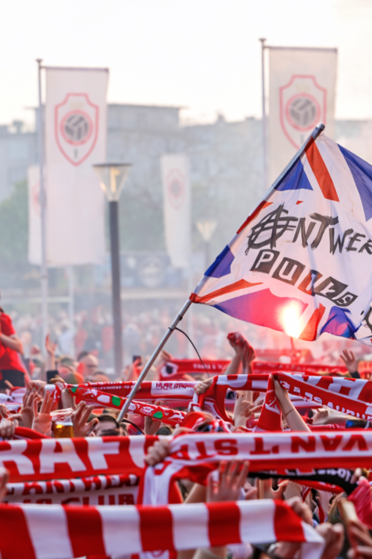Eine große Menge von Fans des Royal Antwerp FC feiert begeistert, schwenkt rot-weiße Schals und eine Fahne mit der Aufschrift „Antwerp Power“, während roter Rauch im Hintergrund aufsteigt.