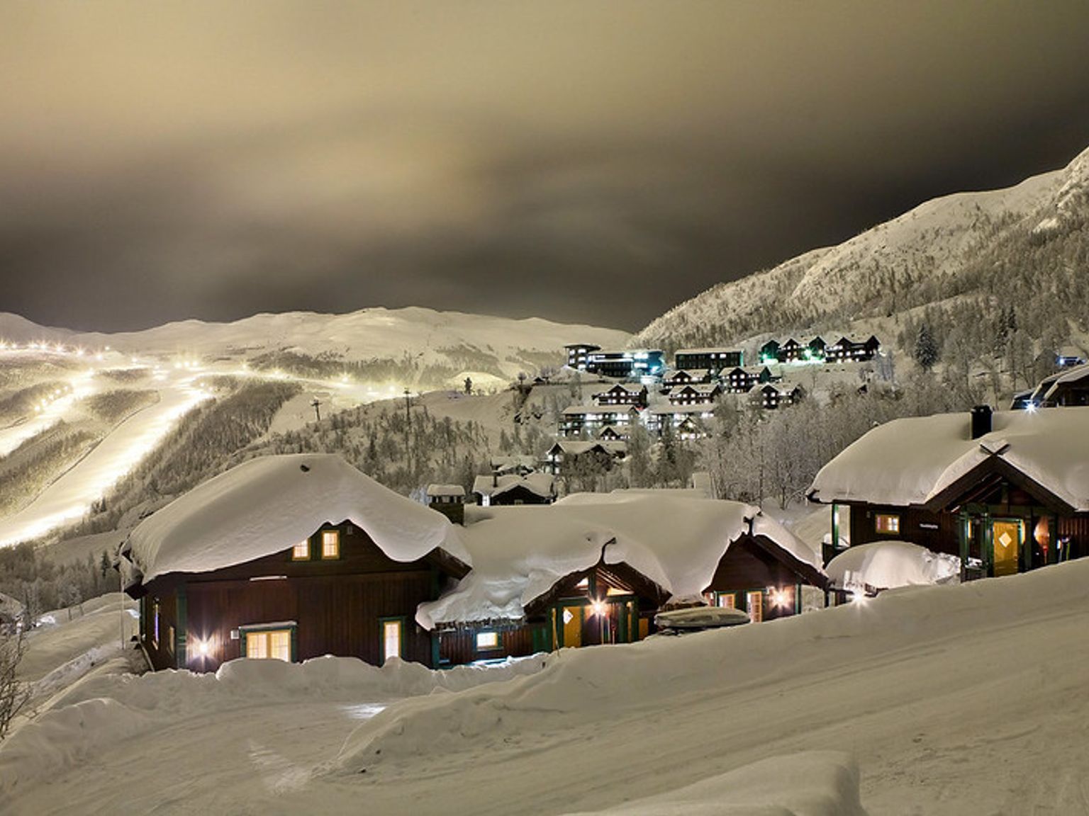 en snødekt landsby med en skiløype i bakgrunnen om natten