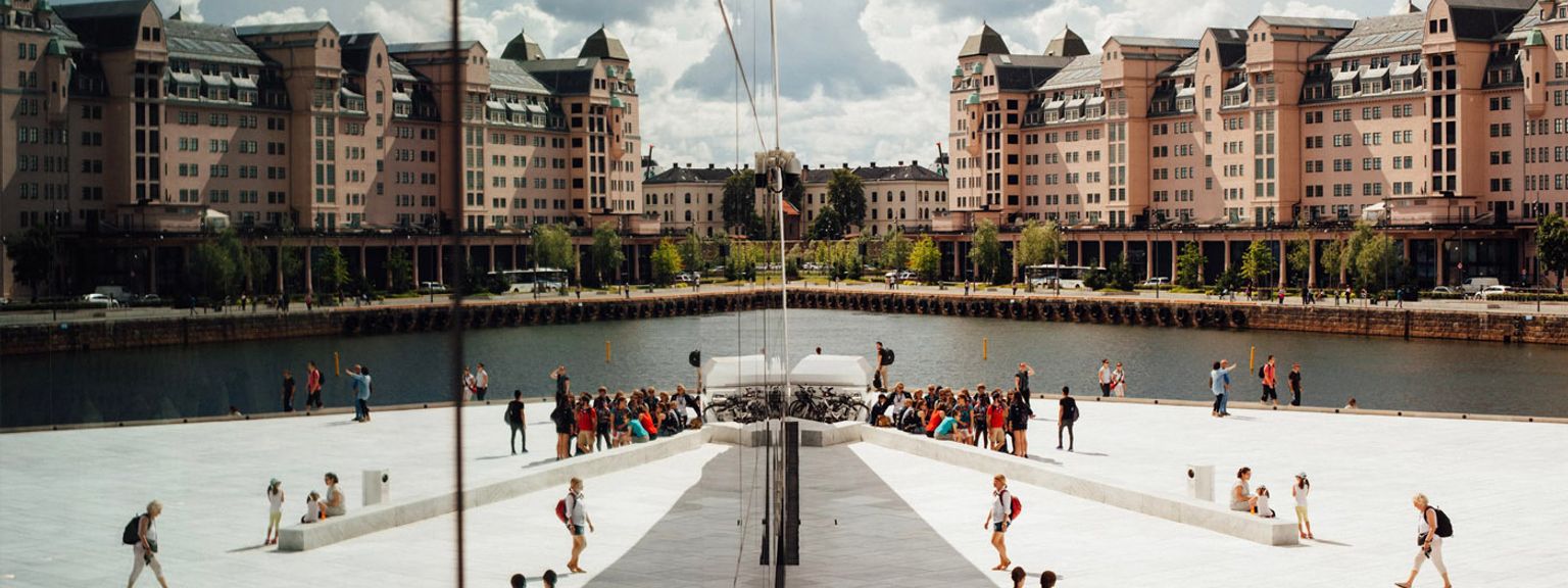 en gruppe mennesker står foran en stor bygning ved siden af et vandområde