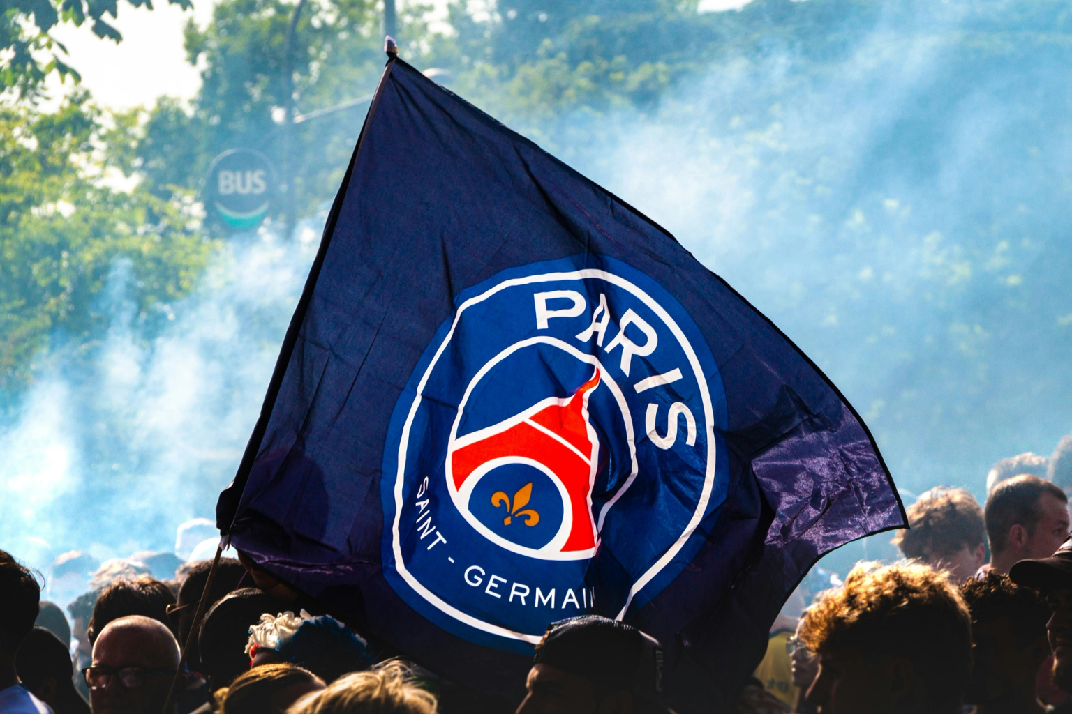En Paris Saint-Germain (PSG) flagga vajar över en folkmassa bland rök.