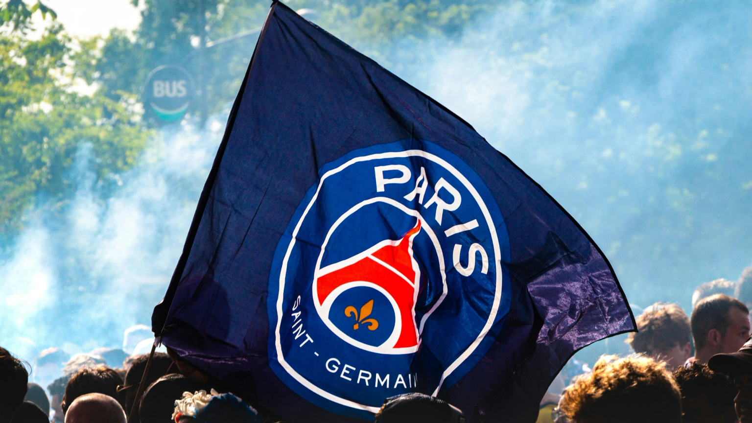 En Paris Saint-Germain (PSG) flagga vajar över en folkmassa bland rök.