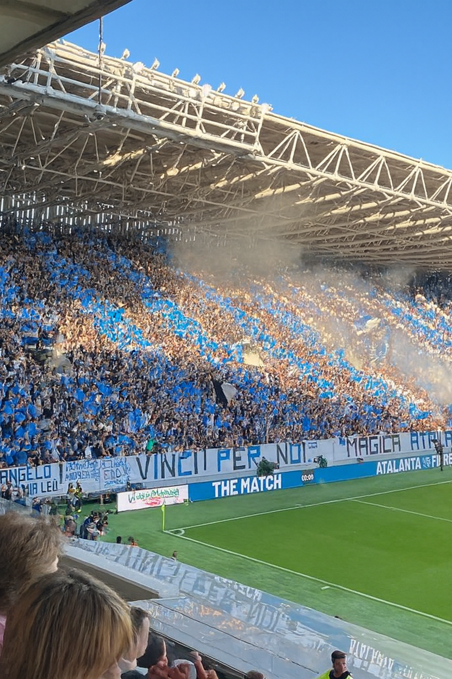 Täynnä oleva jalkapallostadion, joka on täynnä sinisiin pukeutuneita faneja, savua nousee katsomoista ja vihreä kenttä.