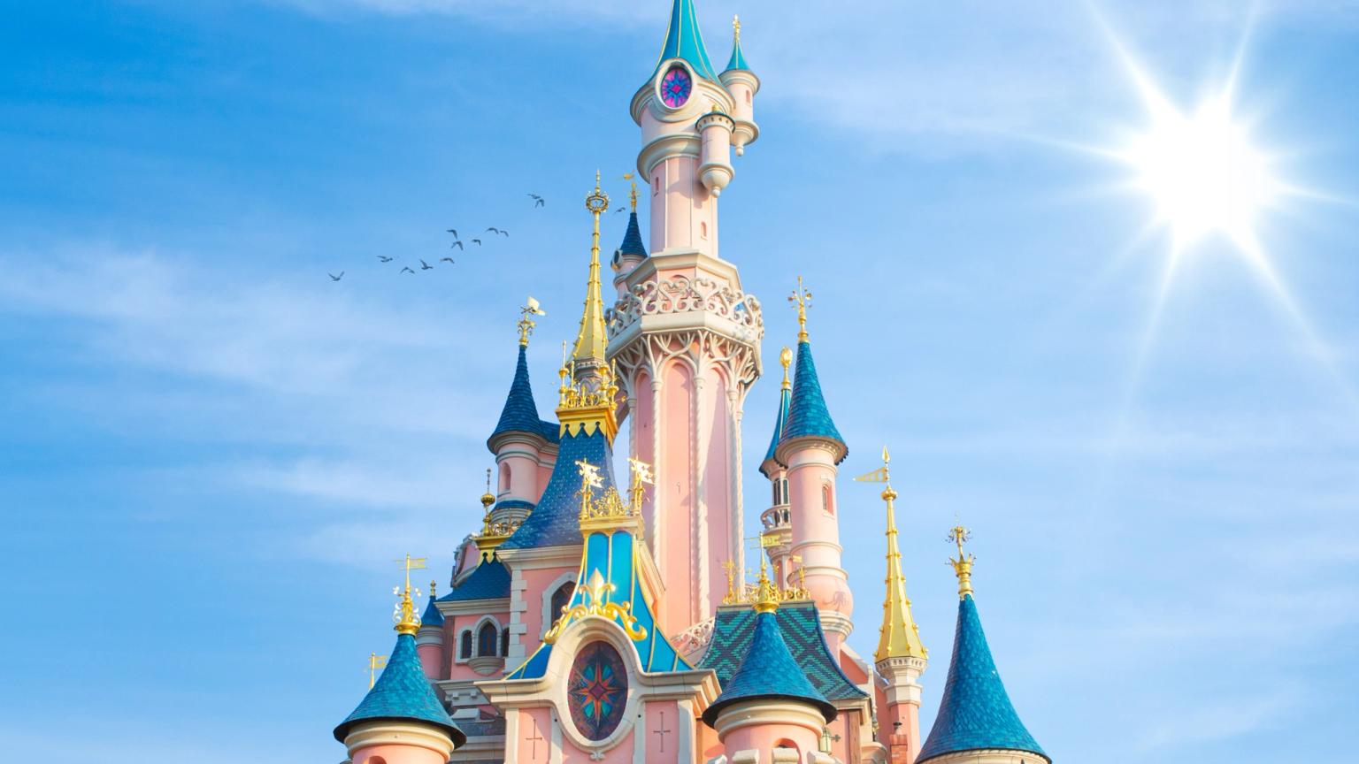 ett stort rosa och blått slott mot en blå himmel med solen som skiner genom molnen