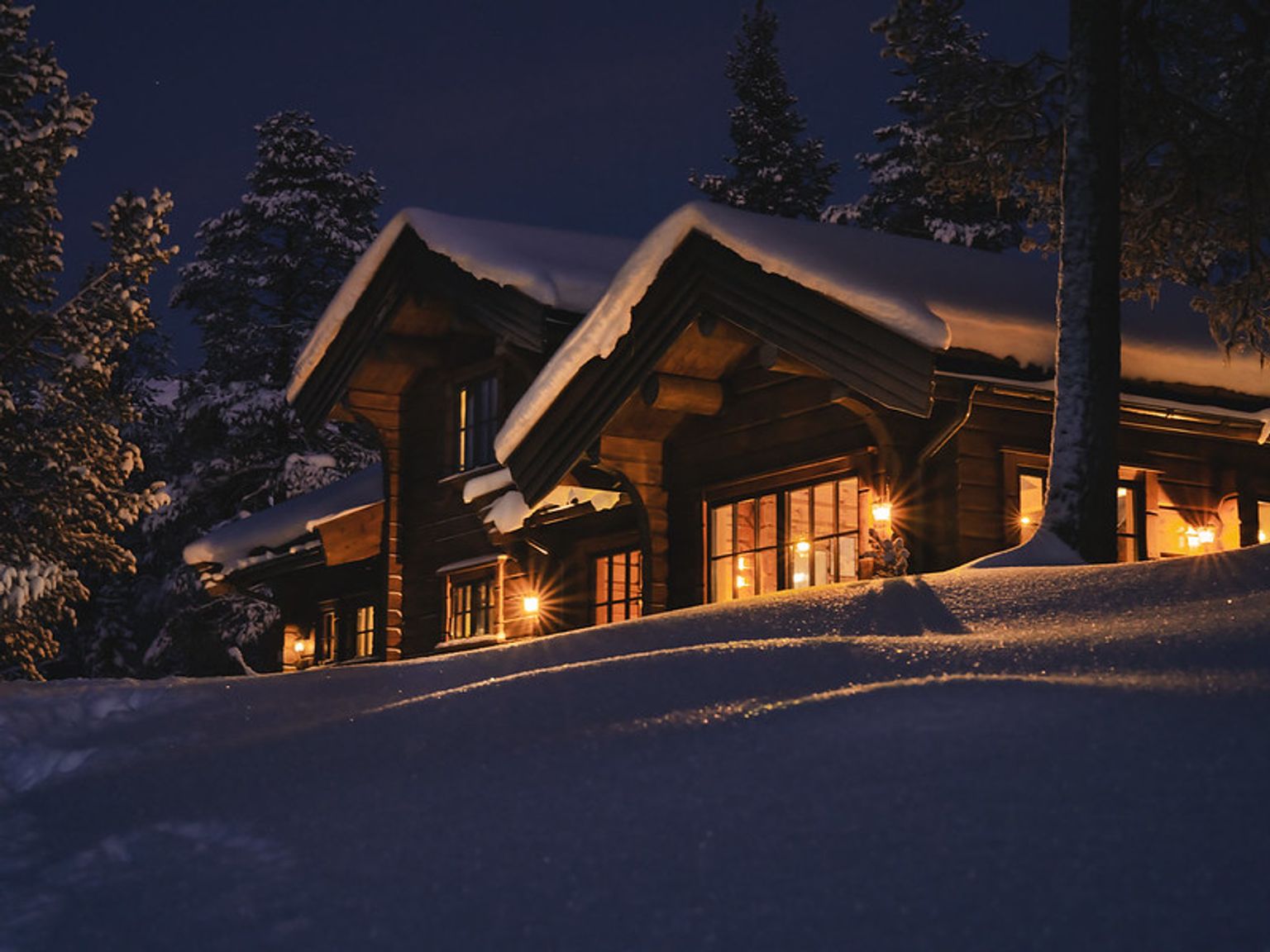 en bjælkehytte er oplyst om natten i sneen.