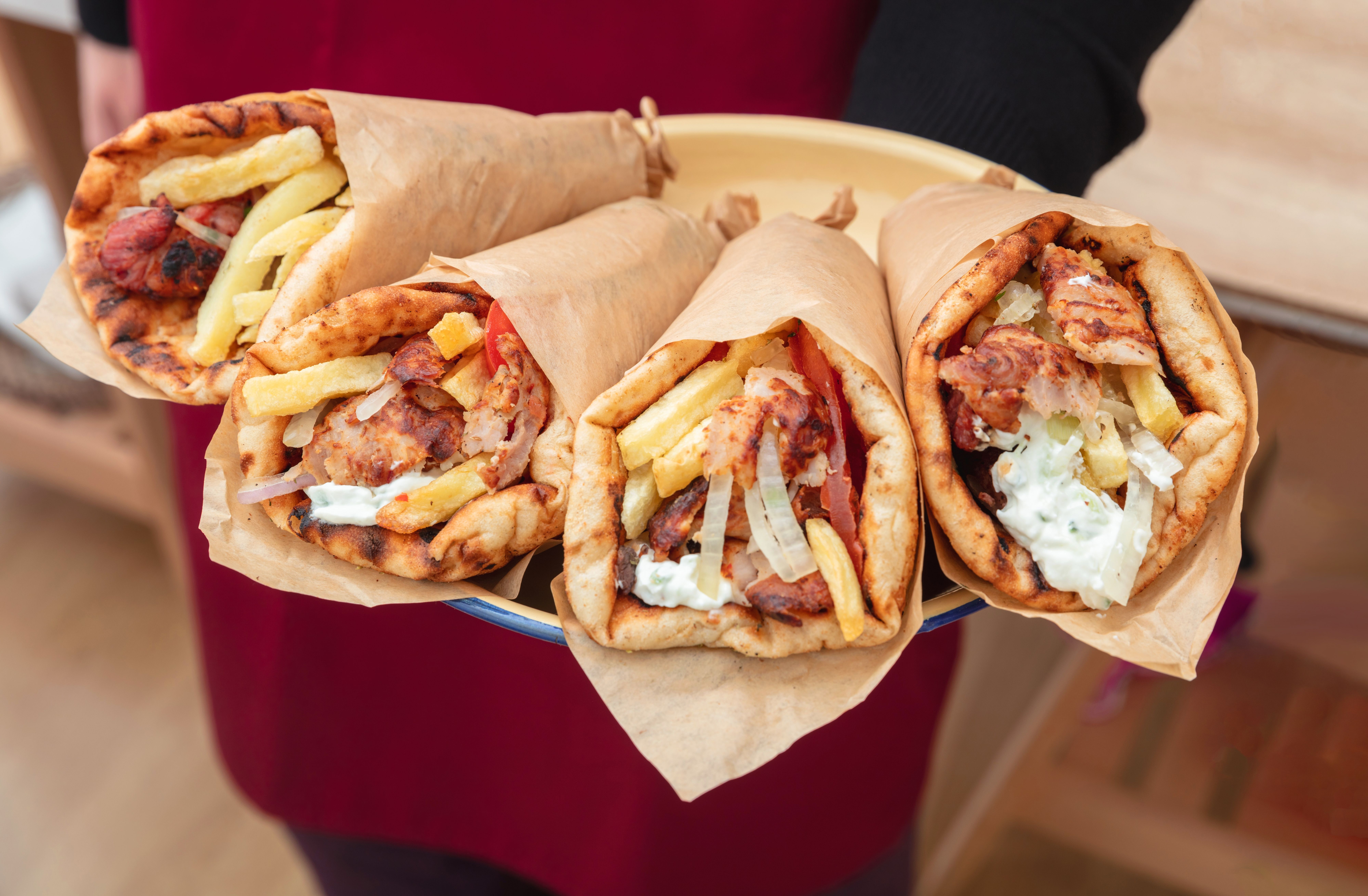 a person is holding a plate of gyros with french fries