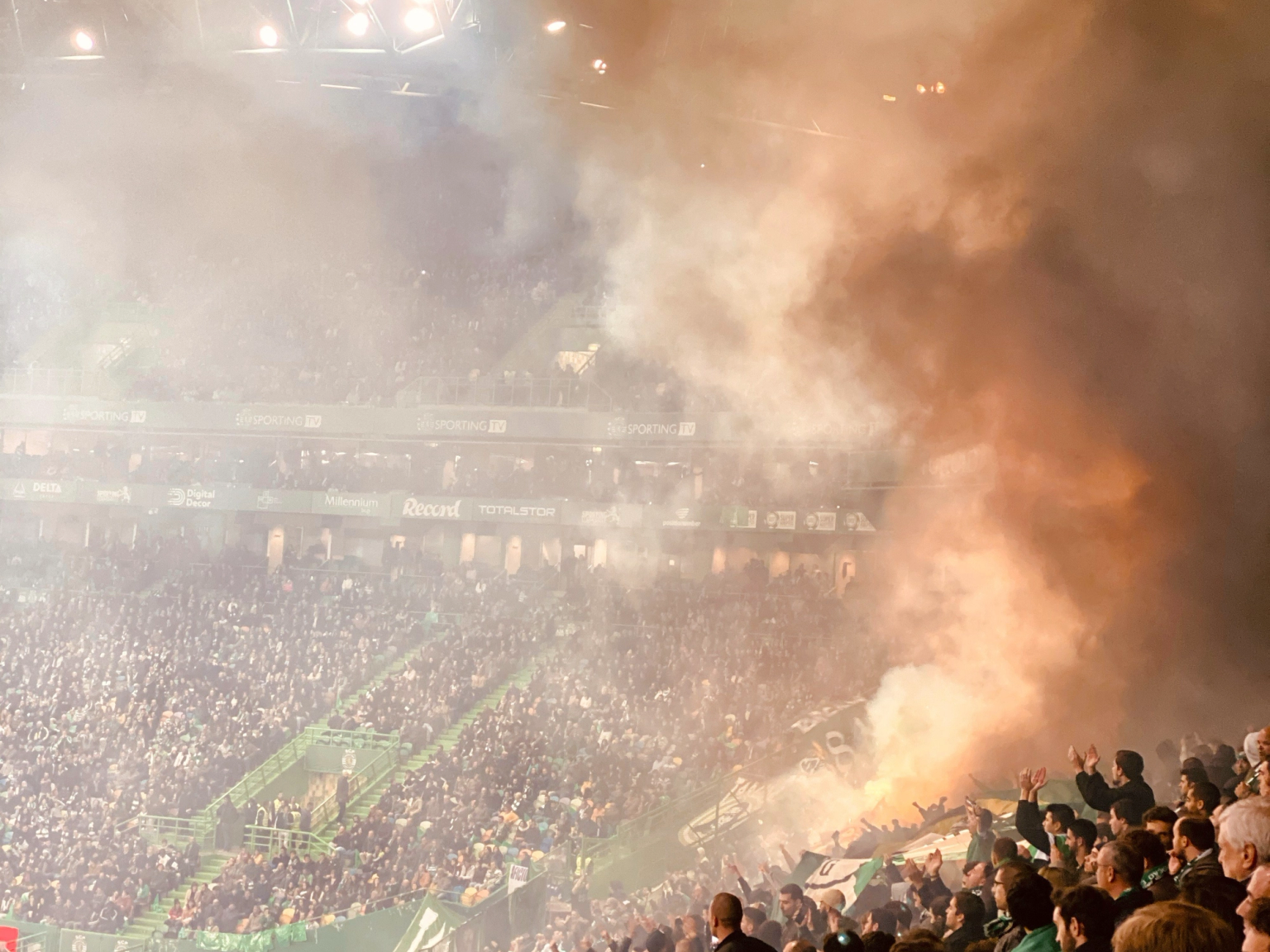 Täynnä oleva stadion, joka on täynnä paksua oranssia ja valkoista savua soihduista.
