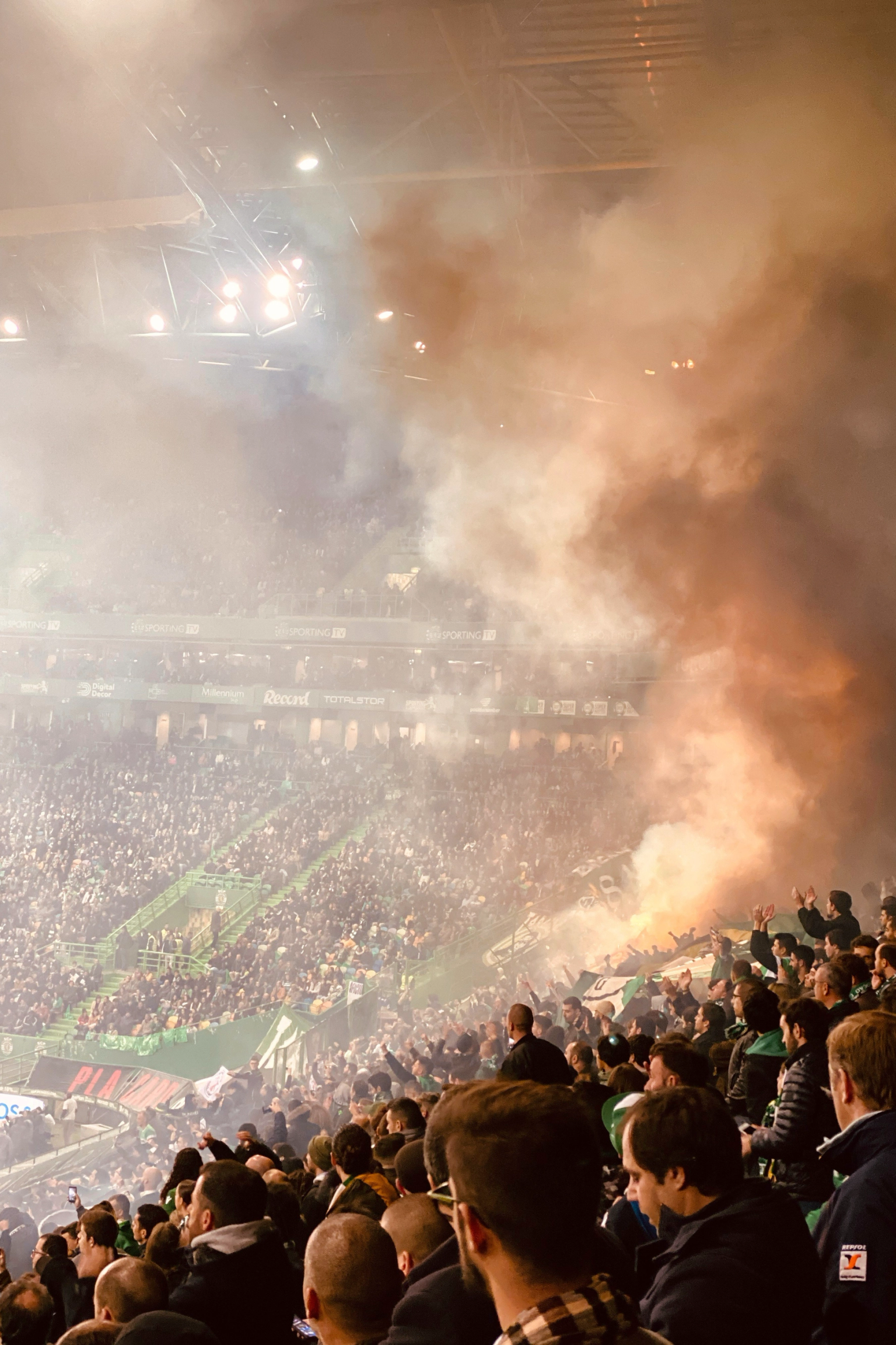Täynnä oleva stadion, joka on täynnä paksua oranssia ja valkoista savua soihduista.