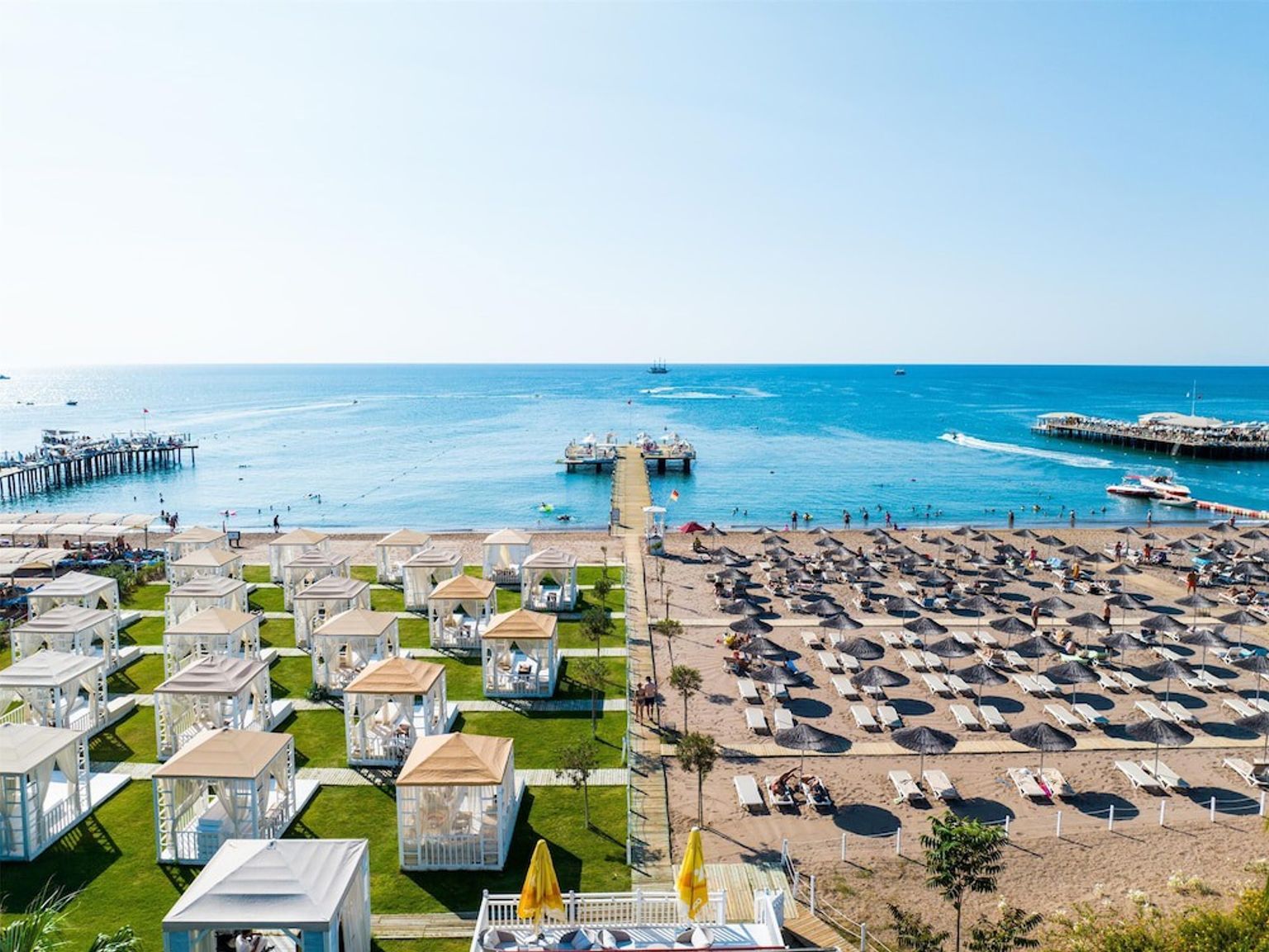 Et solrigt strandresort med to moler, et græsareal med cabanas og en sandstrand med parasoller og liggestole. Aska Lara Resort & Spa