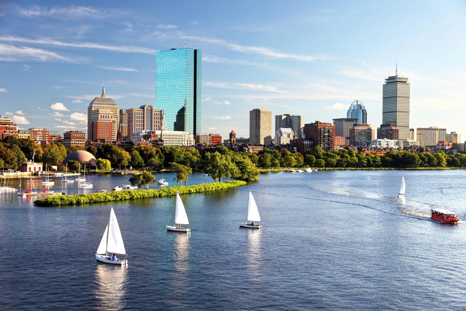 Bostons skyline på den anden side af Charles River med sejlbåde og en rød turistbåd.