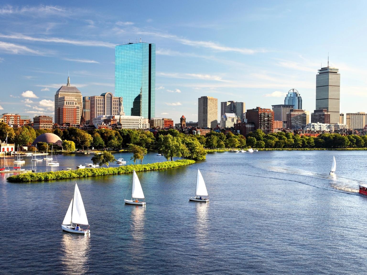 Bostons skyline på den anden side af Charles River med sejlbåde og en rød turistbåd.