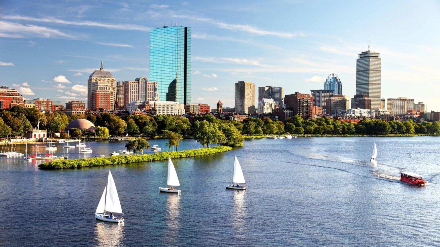 Bostons skyline på den anden side af Charles River med sejlbåde og en rød turistbåd.