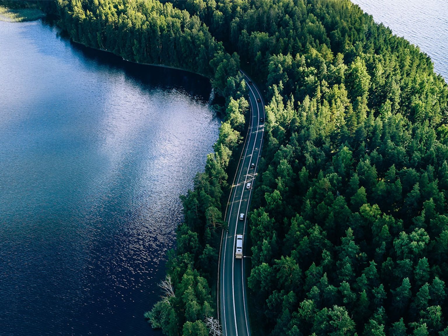 en flygvy över en väg omgiven av träd och en sjö