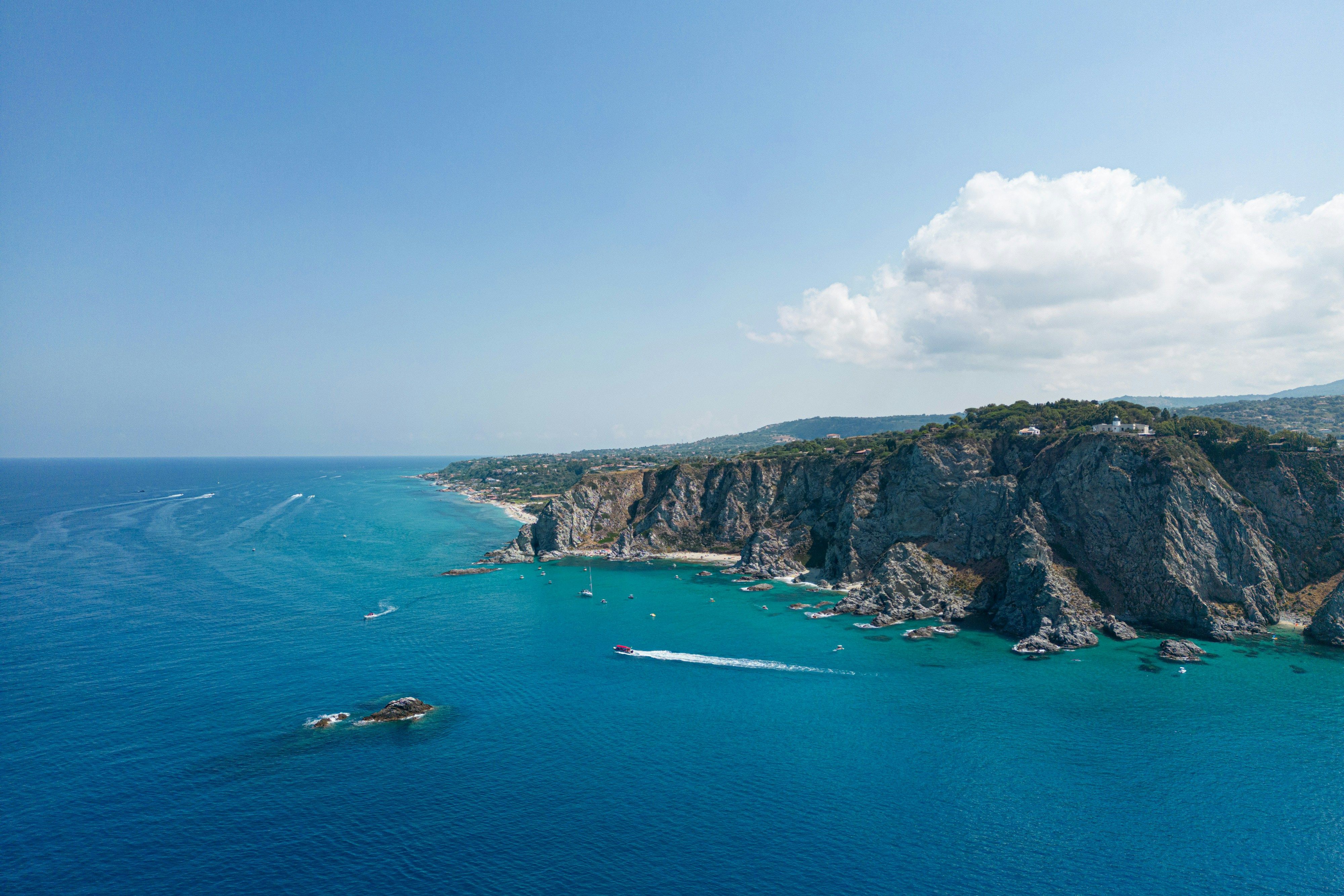 Luftfoto av en livlig kystlinje med dramatiske klipper, en sandstrand og klart blått vann med båter. Capo Vaticano, Italia
