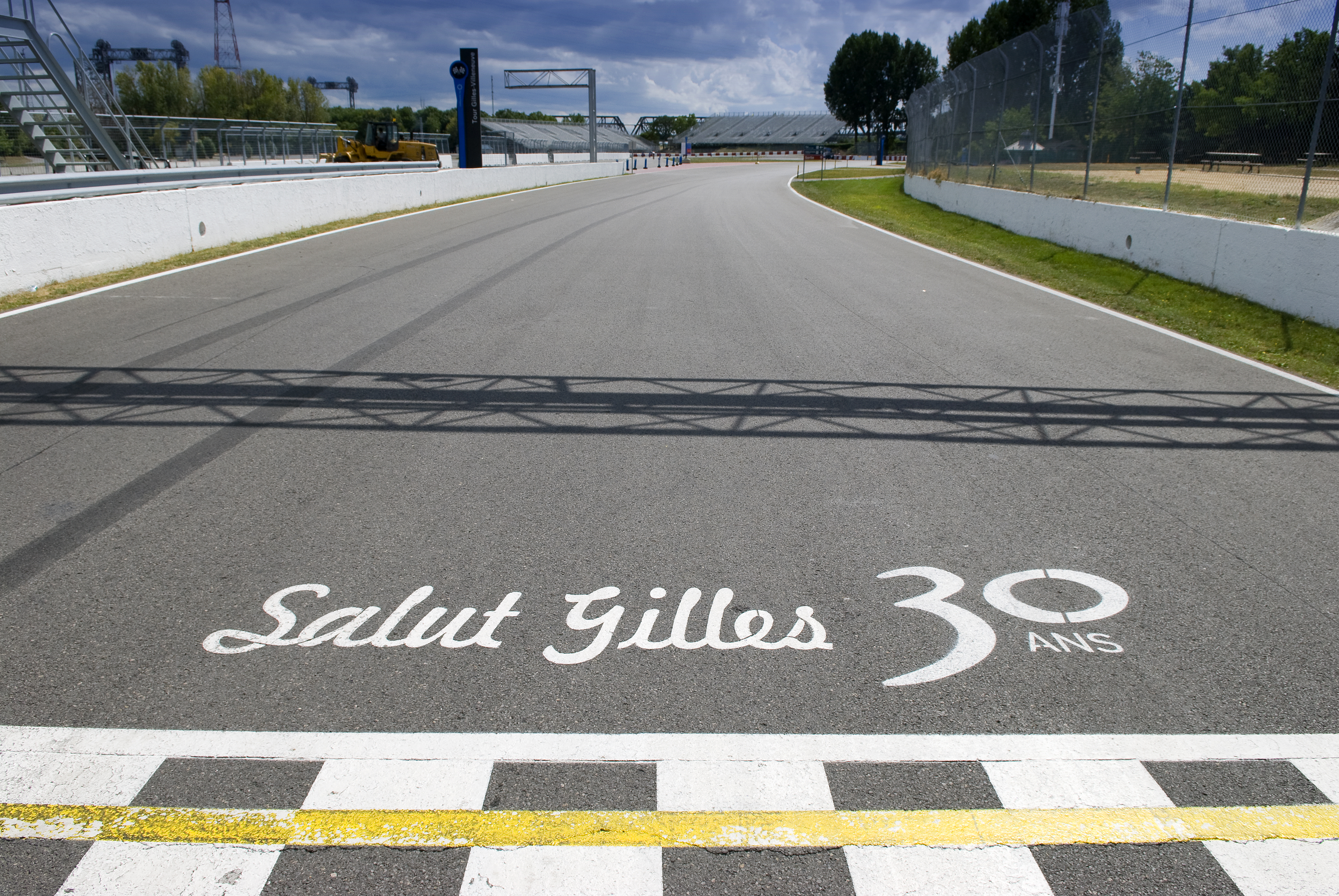 Tor wyścigowy z szachownicową linią mety oraz napisem „Salut Gilles 30 ANS” namalowanym na asfalcie.