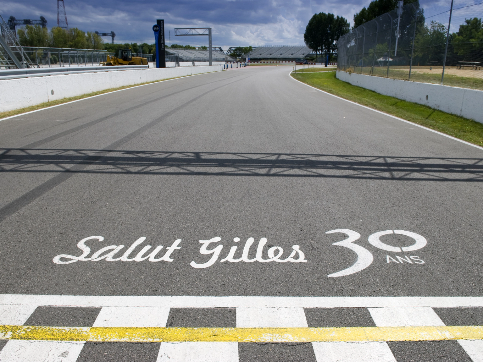 Tor wyścigowy z szachownicową linią mety oraz napisem „Salut Gilles 30 ANS” namalowanym na asfalcie.