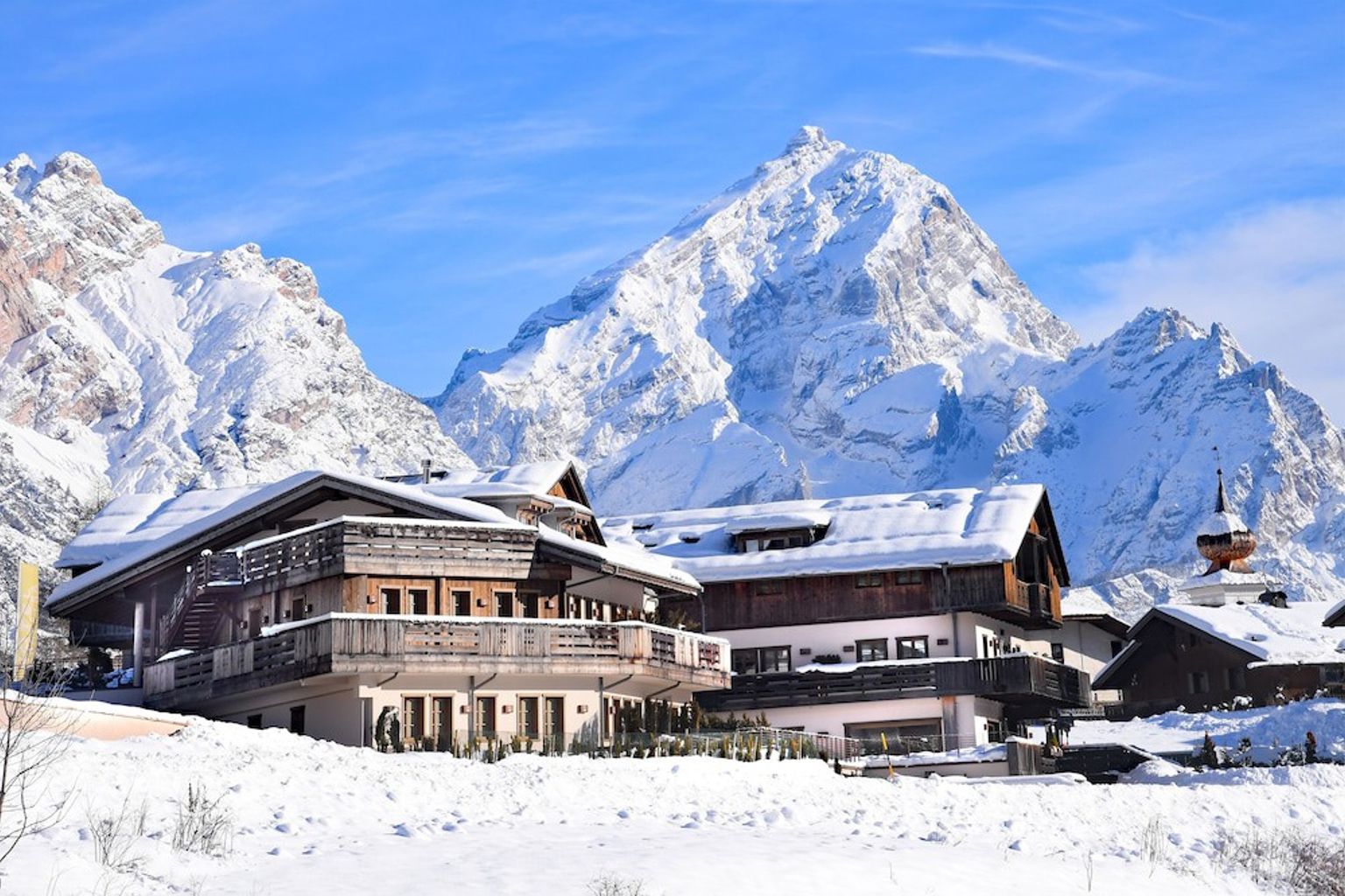 een groot gebouw bedekt met sneeuw met een berg op de achtergrond. Rosapetra Spa Resort, Cortina d’Ampezzo