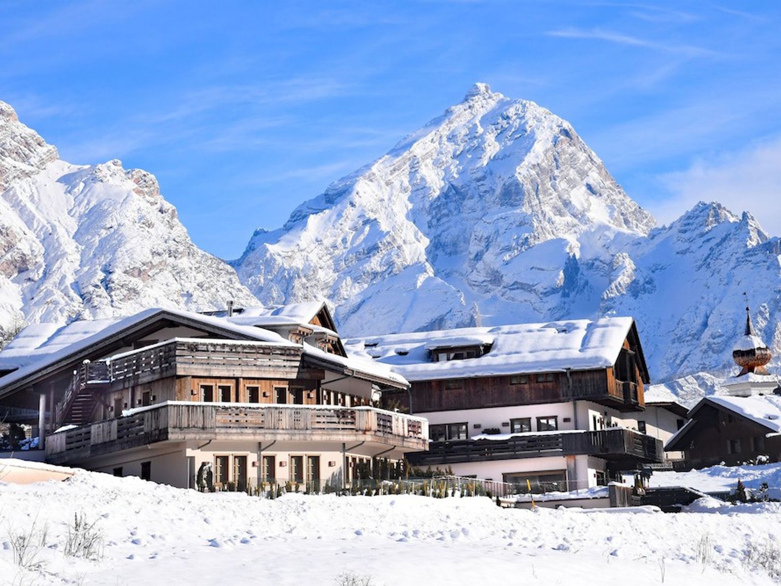 en stor bygning dekket av snø med et fjell i bakgrunnen. Rosapetra Spa Resort, Cortina d’Ampezzo
