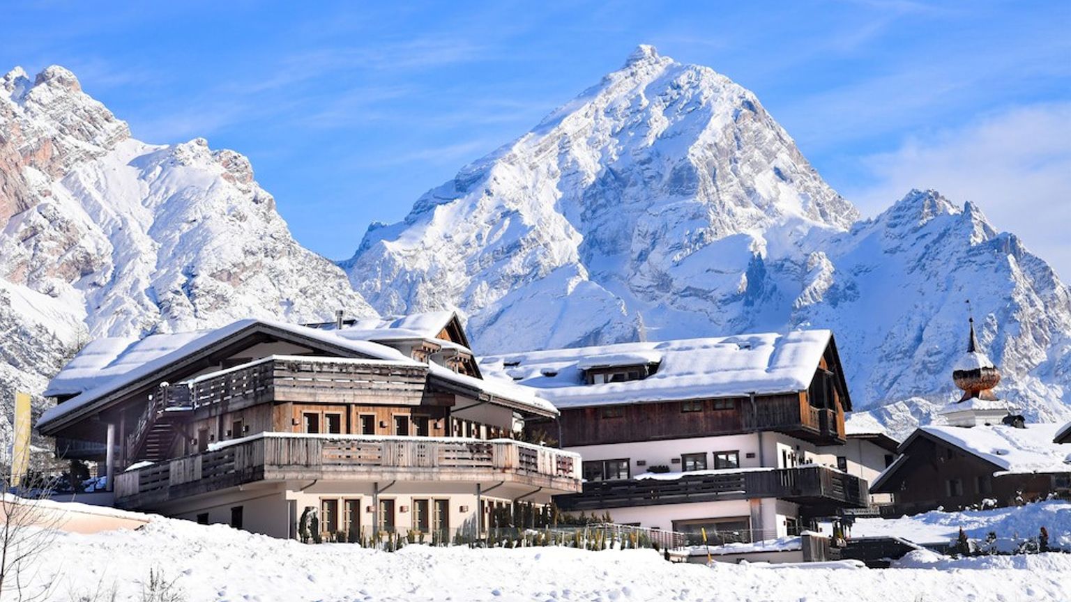 een groot gebouw bedekt met sneeuw met een berg op de achtergrond. Rosapetra Spa Resort, Cortina d’Ampezzo