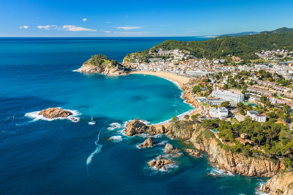 Luftfoto af en kystby med en sandstrand, turkis vand og klippefremspring. Tossa de Mar, Spanien