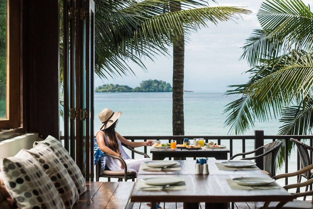 a woman is sitting at a table with a view of the ocean